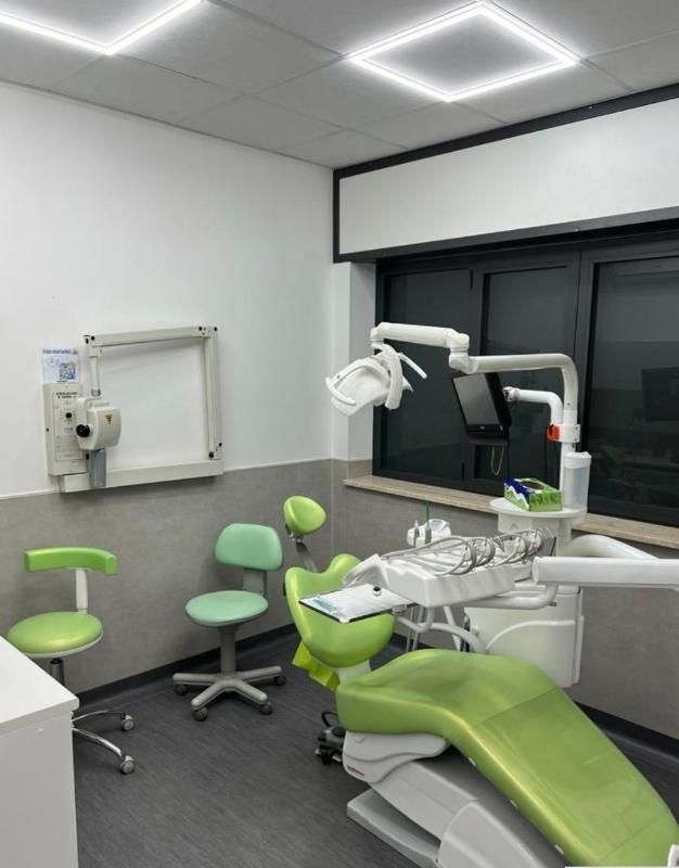Poltrona odontoiatrica verde brillante in una moderna sala visite con sgabelli abbinati e lampada a soffitto vicino a una finestra.