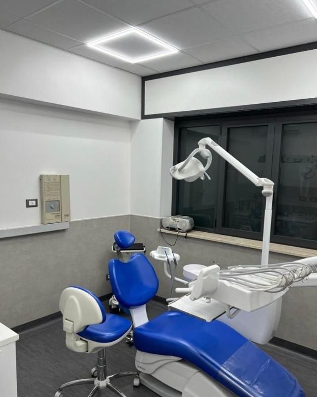 Poltrona odontoiatrica blu e attrezzature in una moderna sala clinica con luci a finestra e a soffitto.