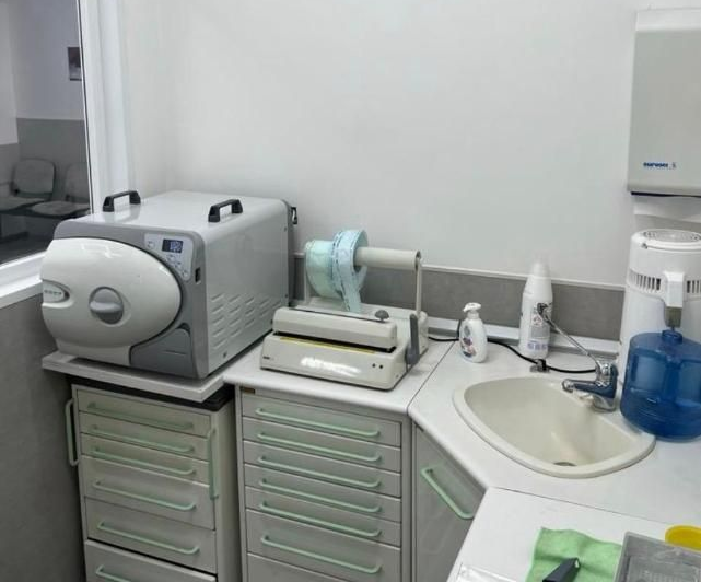 Area lavabo della clinica con sterilizzatore da banco, cassetti e dispenser di sapone blu accanto a un piccolo lavabo.