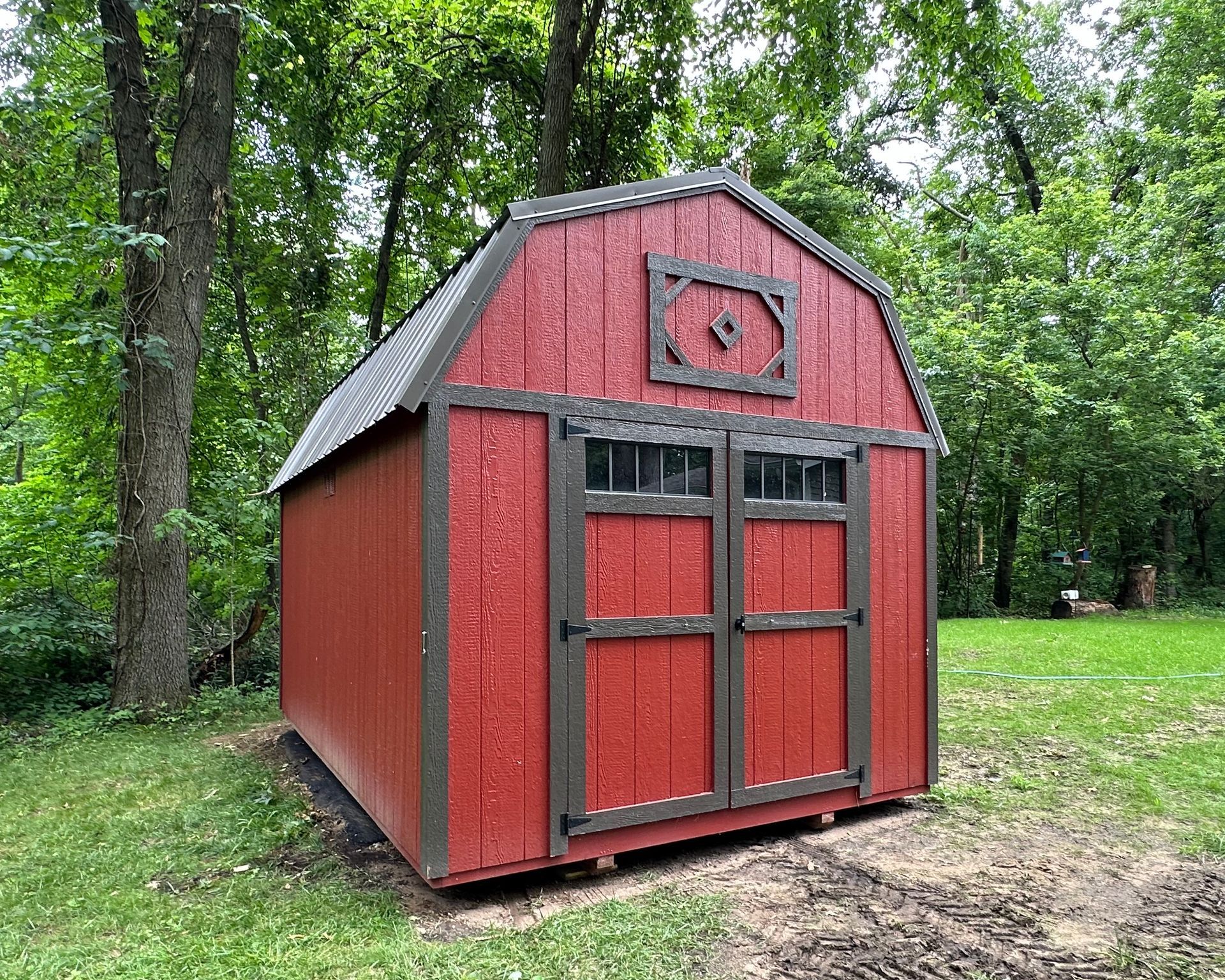 A red barn shed is sitting in the middle of a grassy field.