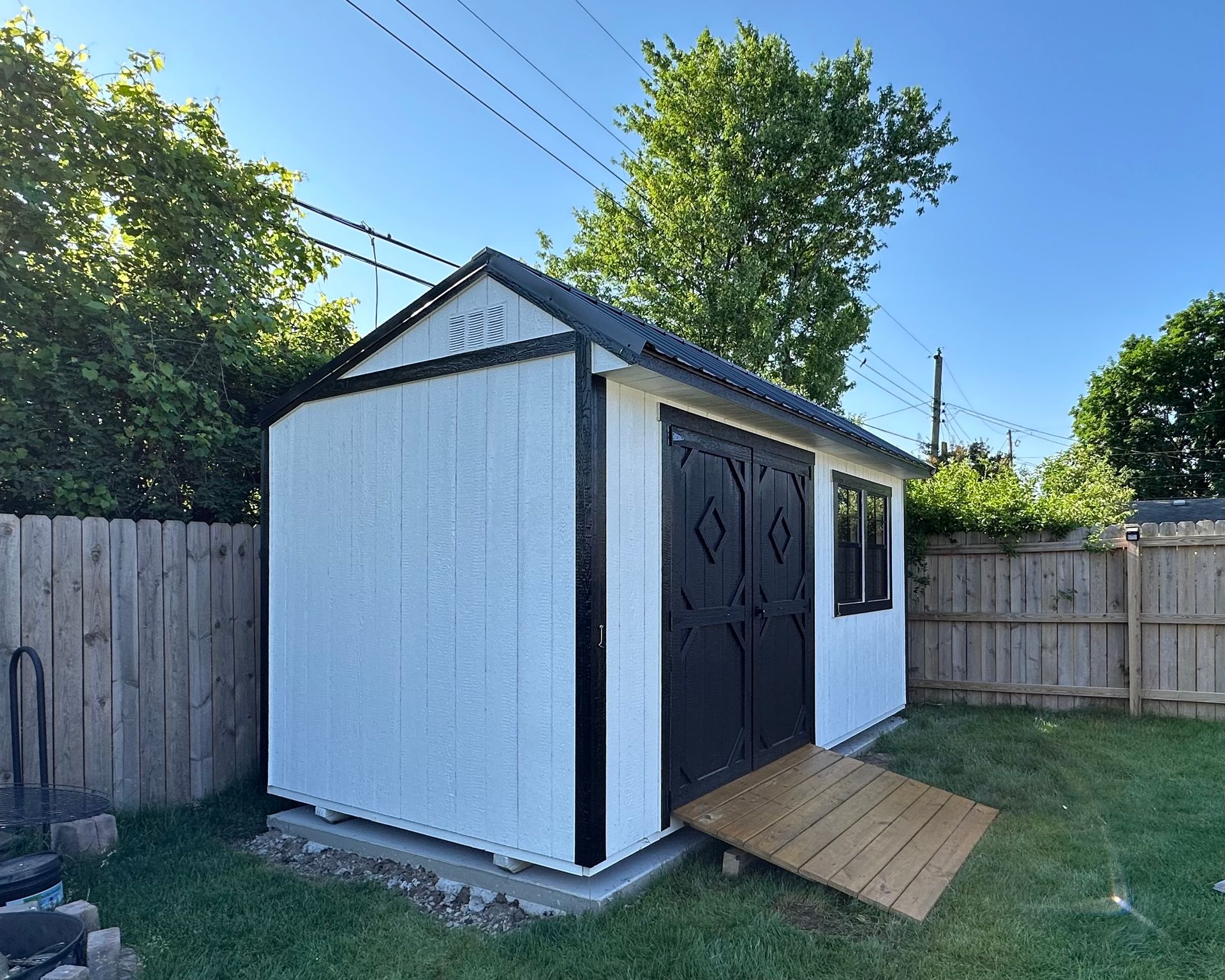 A white and black shed with a ramp in the backyard.