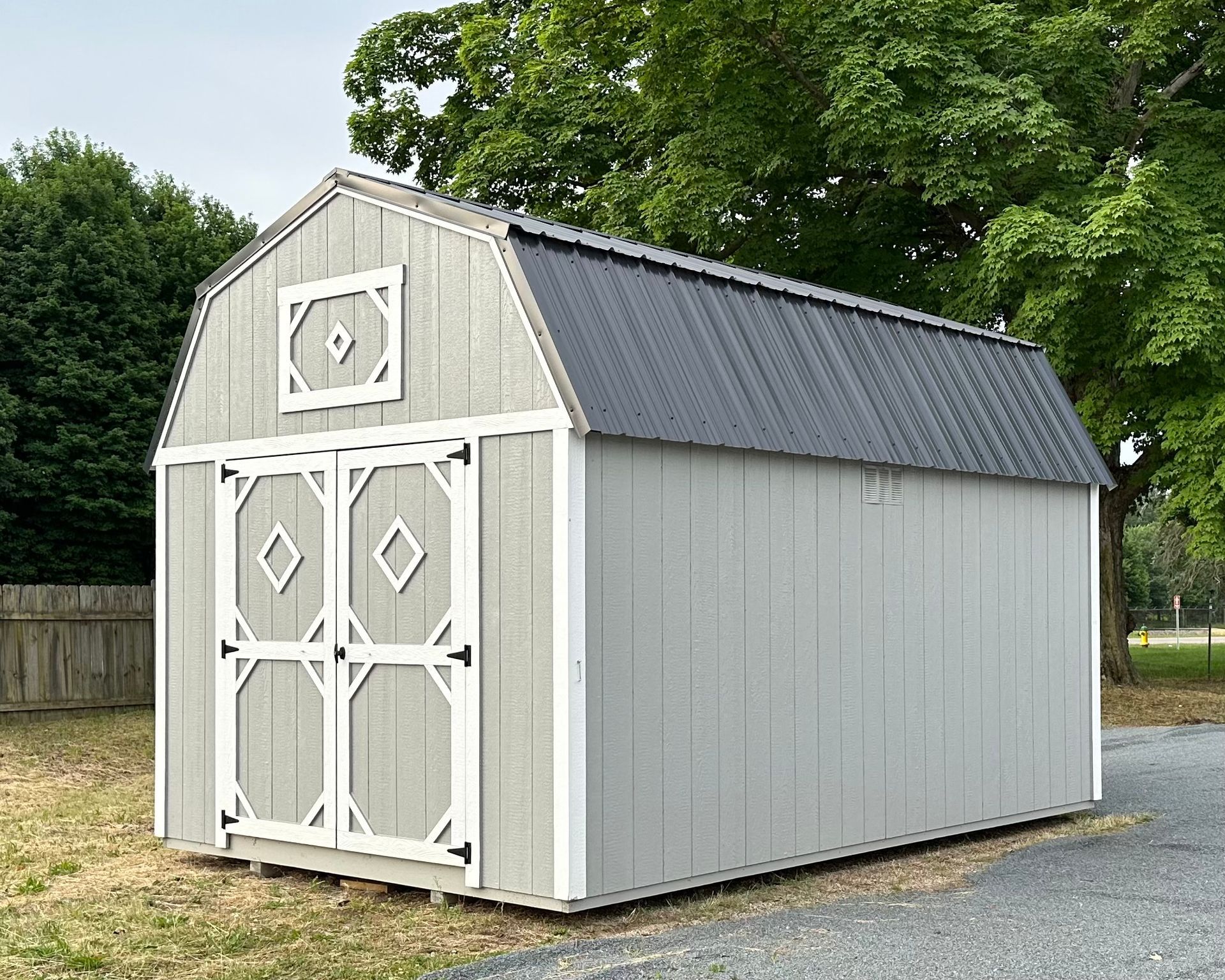 A barn with a black roof is sitting in the middle of a grassy field.