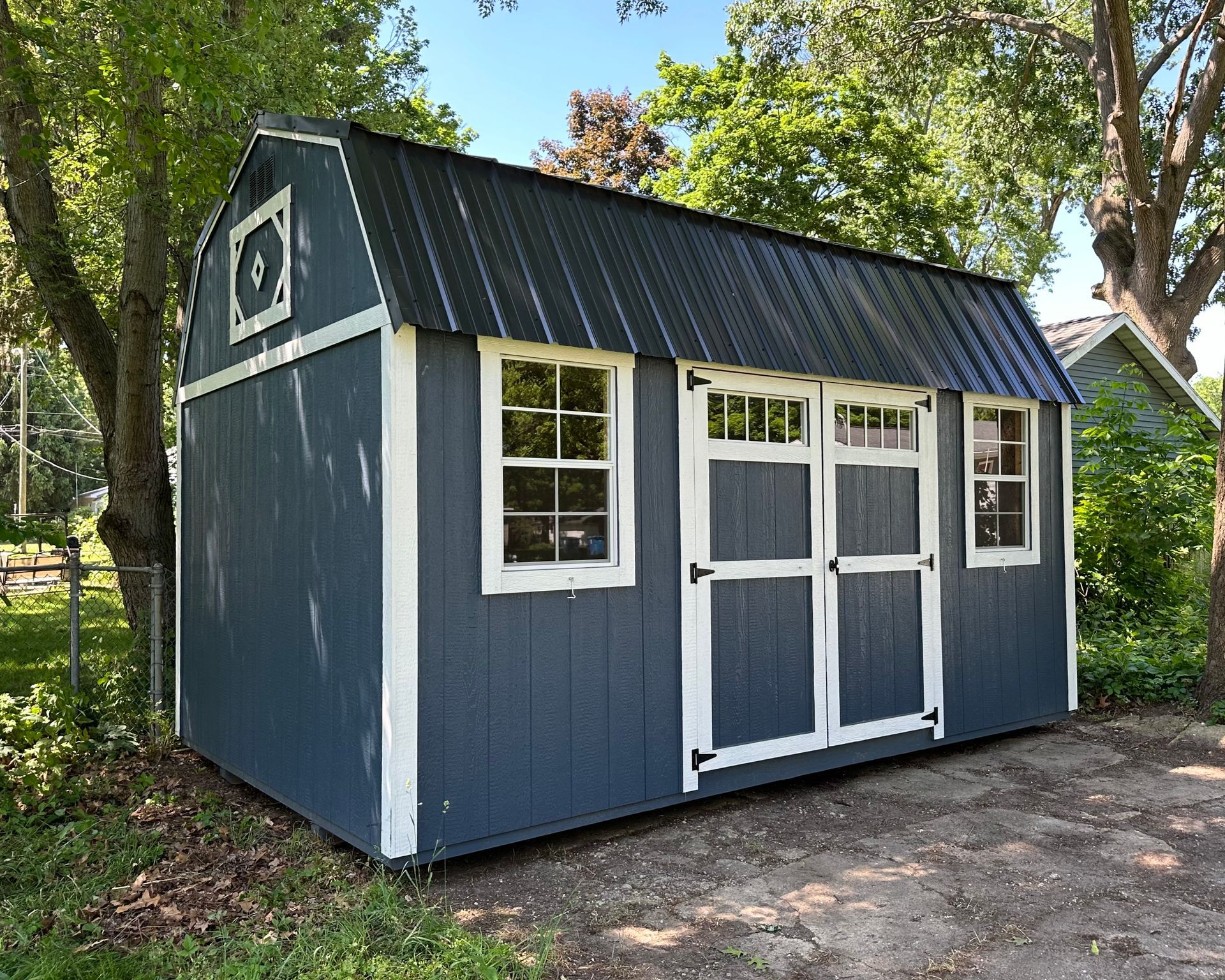 A blue barn shed with a black roof and white trim is sitting in a yard.