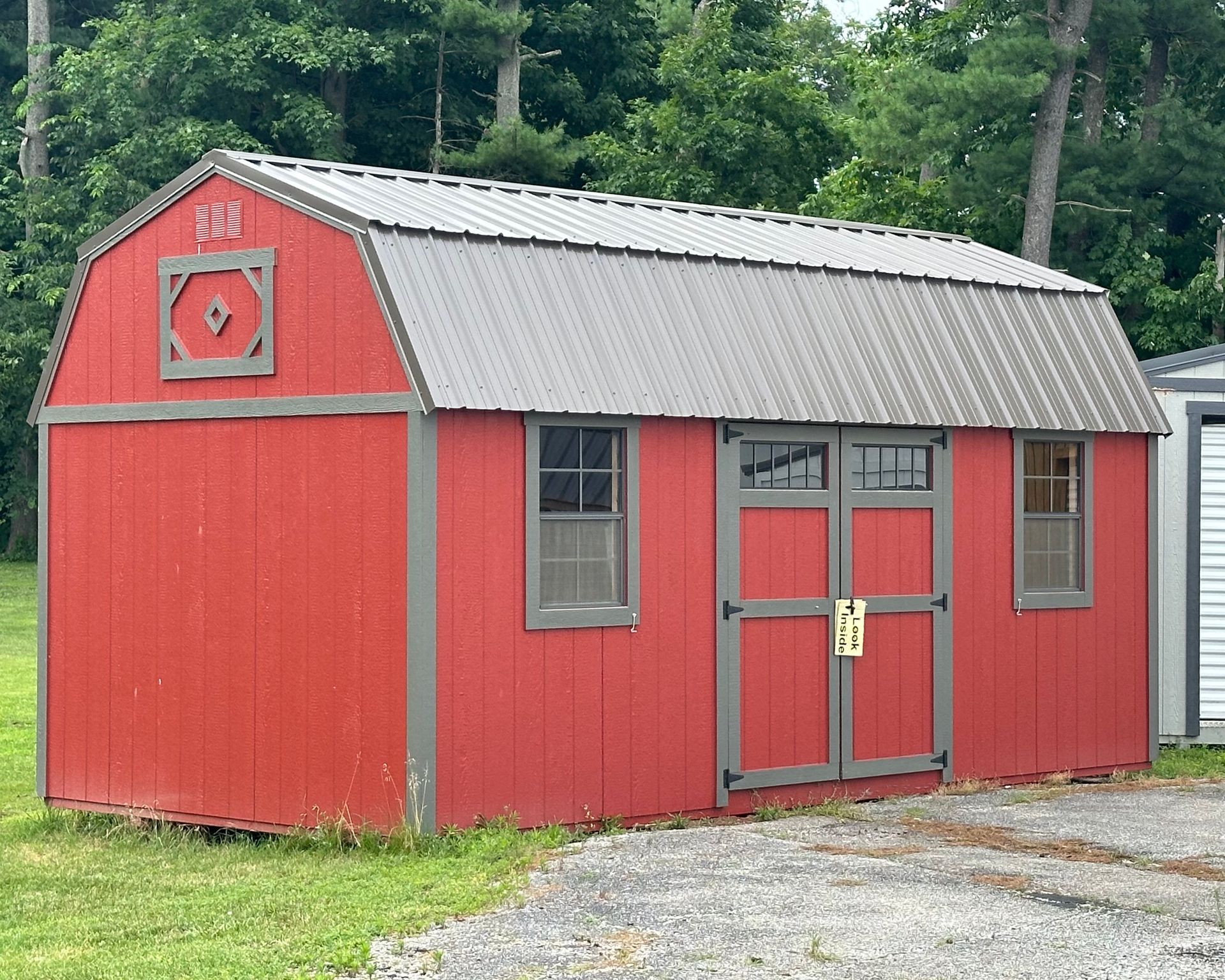 A red barn with a gray roof is sitting in a grassy field.
