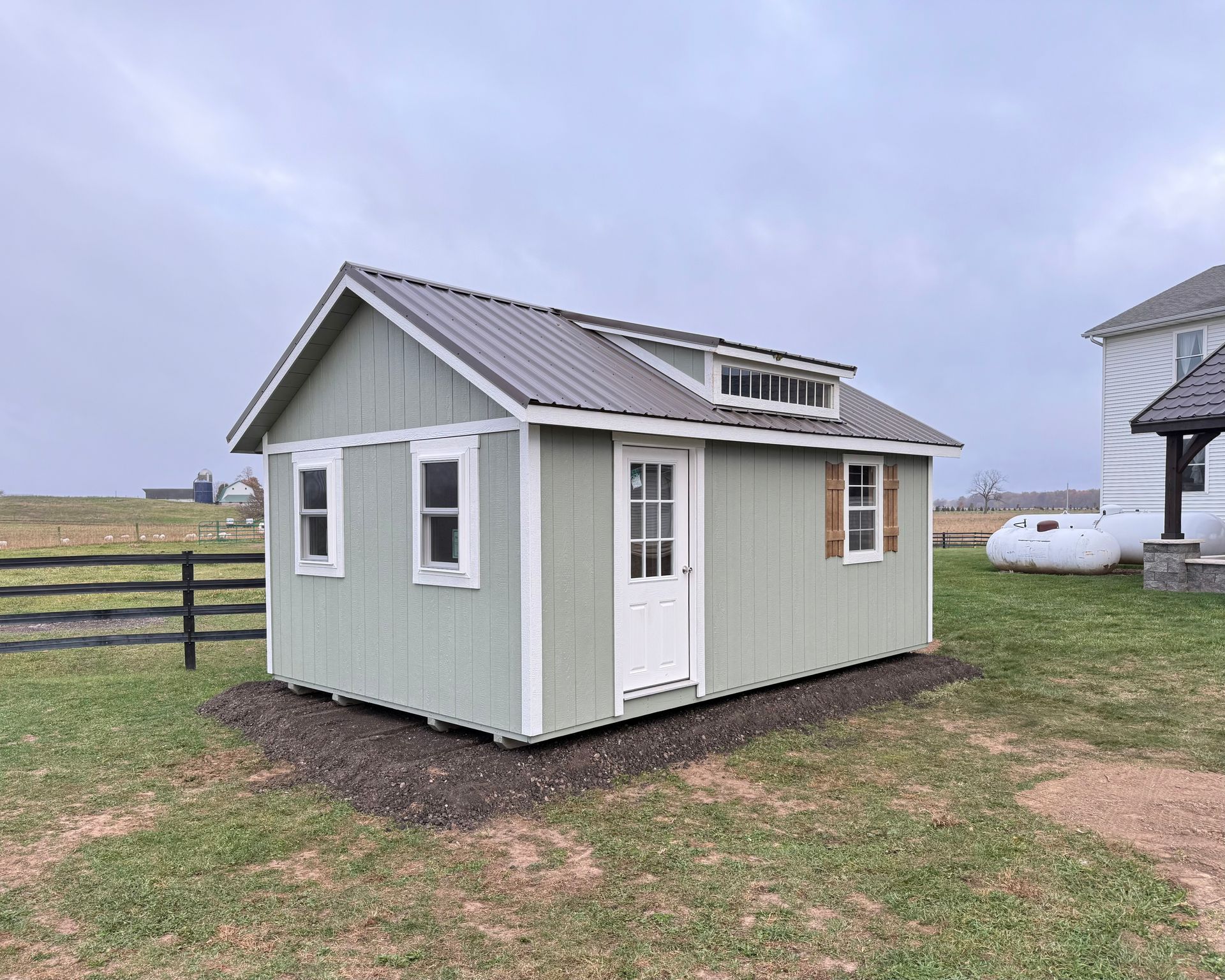 A small green shed is sitting in the middle of a grassy field.
