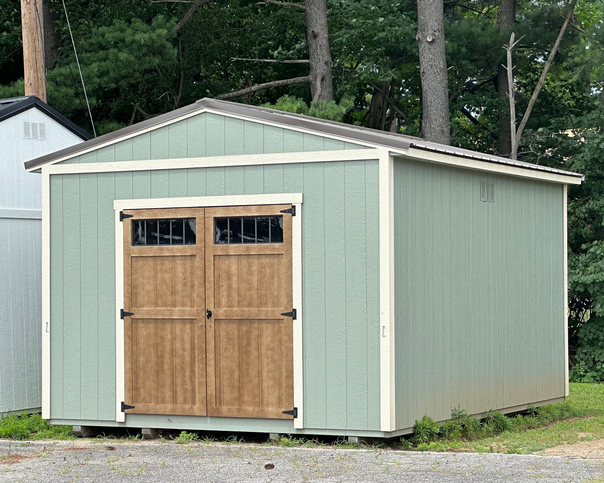 A green shed with wooden doors and windows is sitting in the grass.