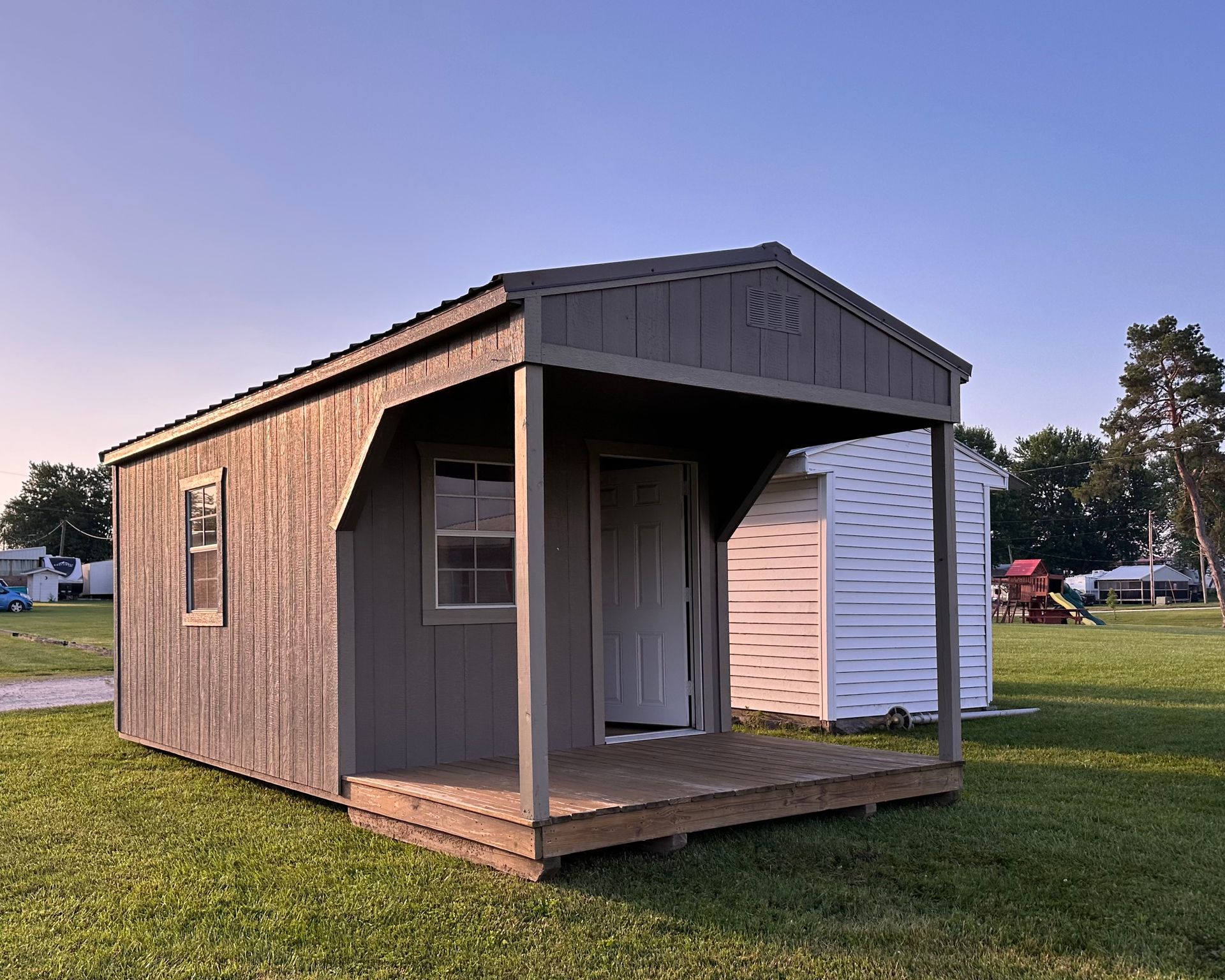 A small shed with a porch is sitting in the middle of a grassy field.