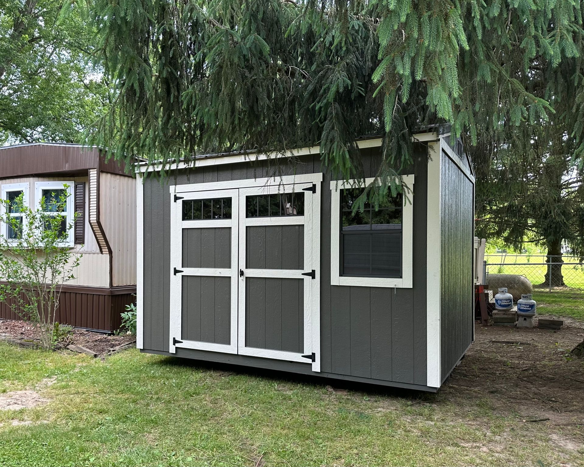 A gray and white shed is sitting in the grass next to a tree.