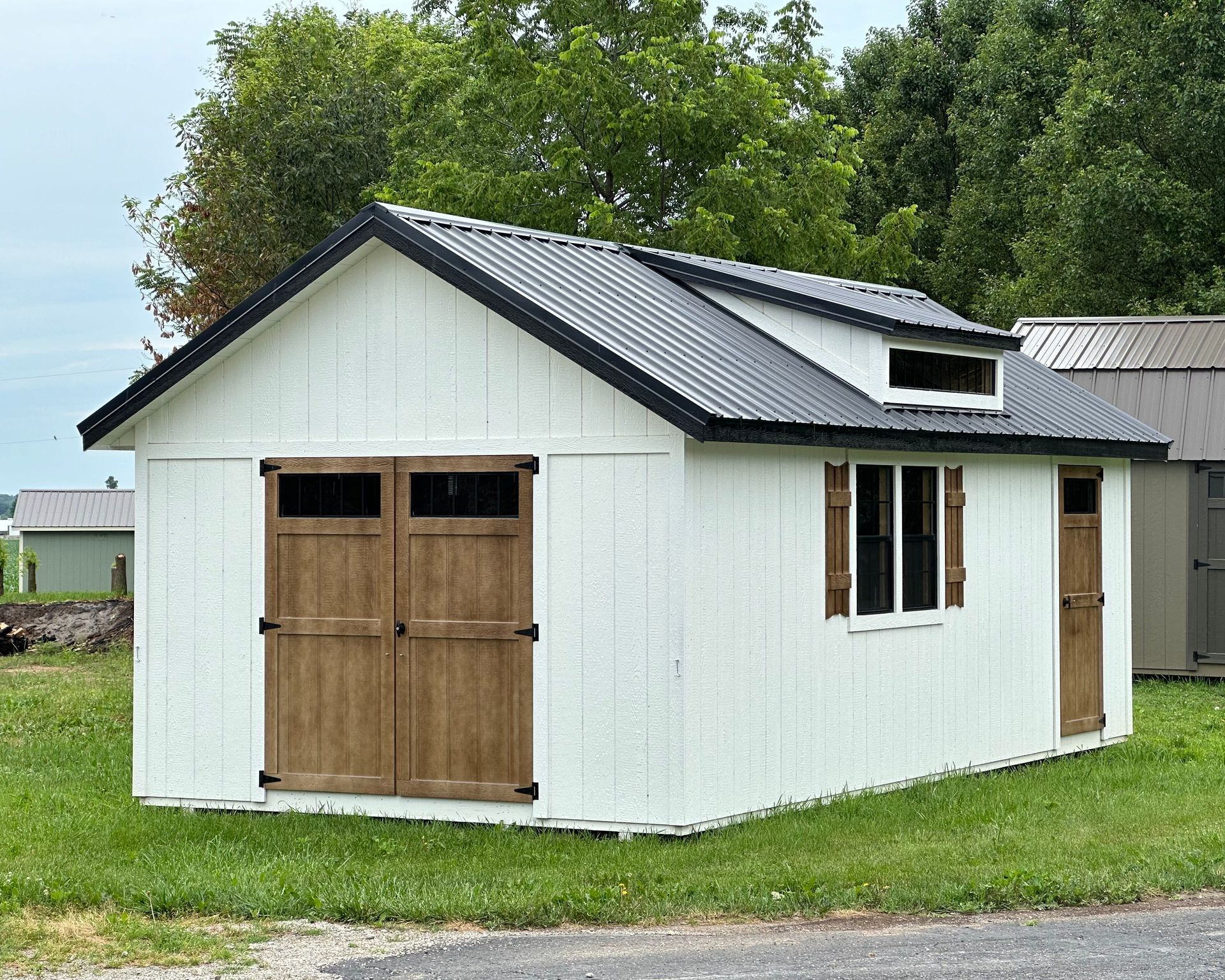 A white shed with a black roof is sitting in the middle of a grassy field.