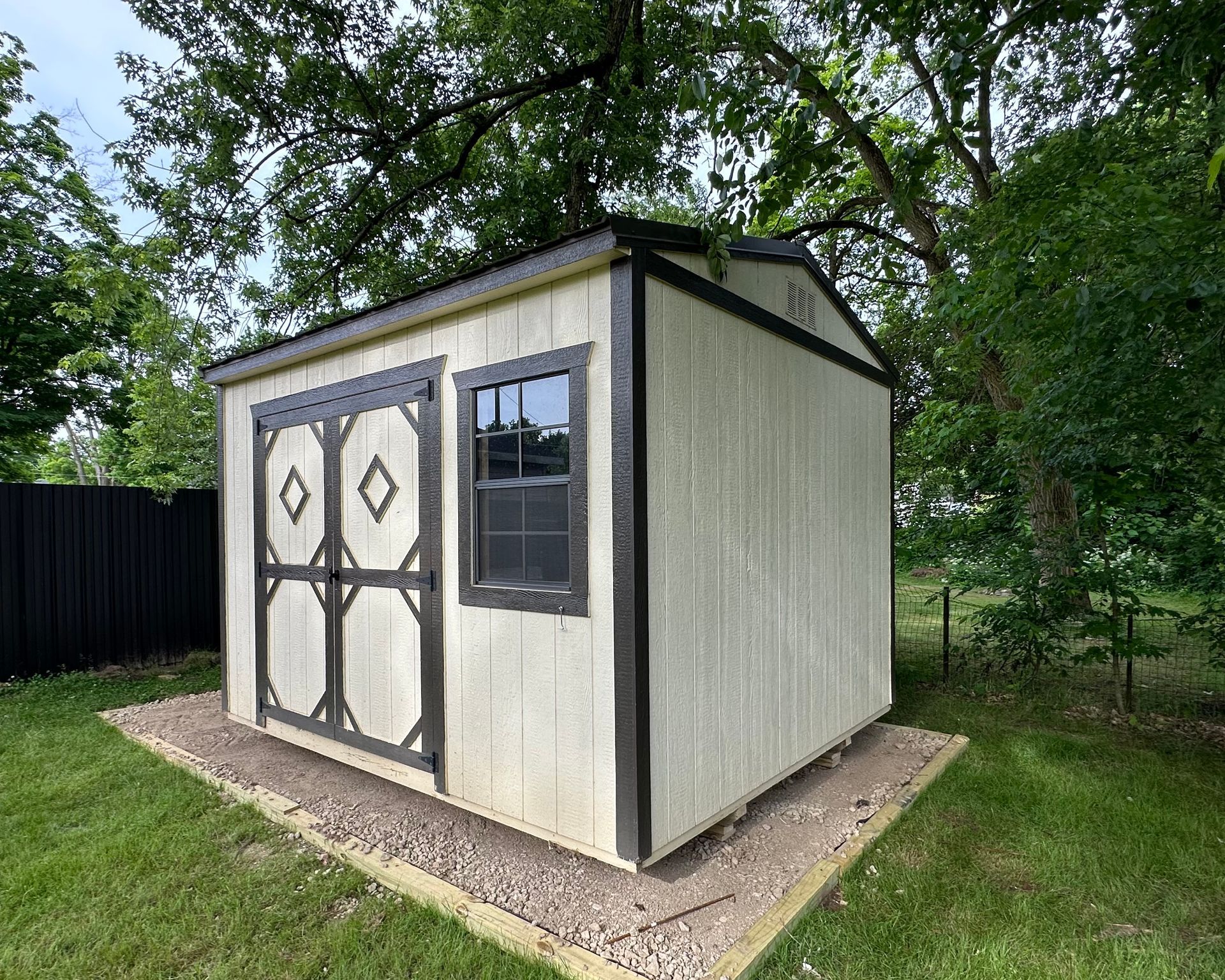 A small white shed with a window is sitting in the middle of a grassy yard.