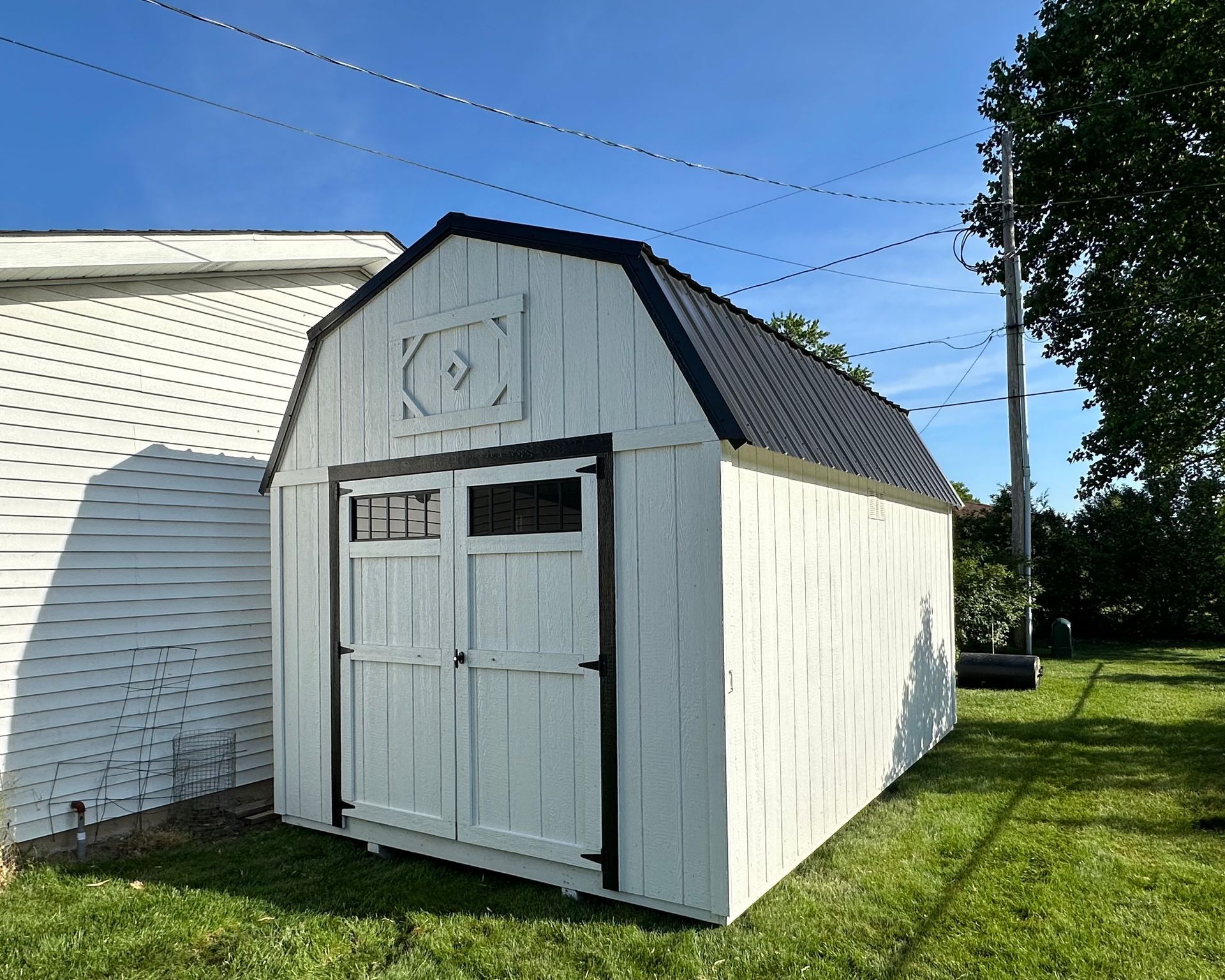 A white barn shed is sitting in the grass next to a white house.