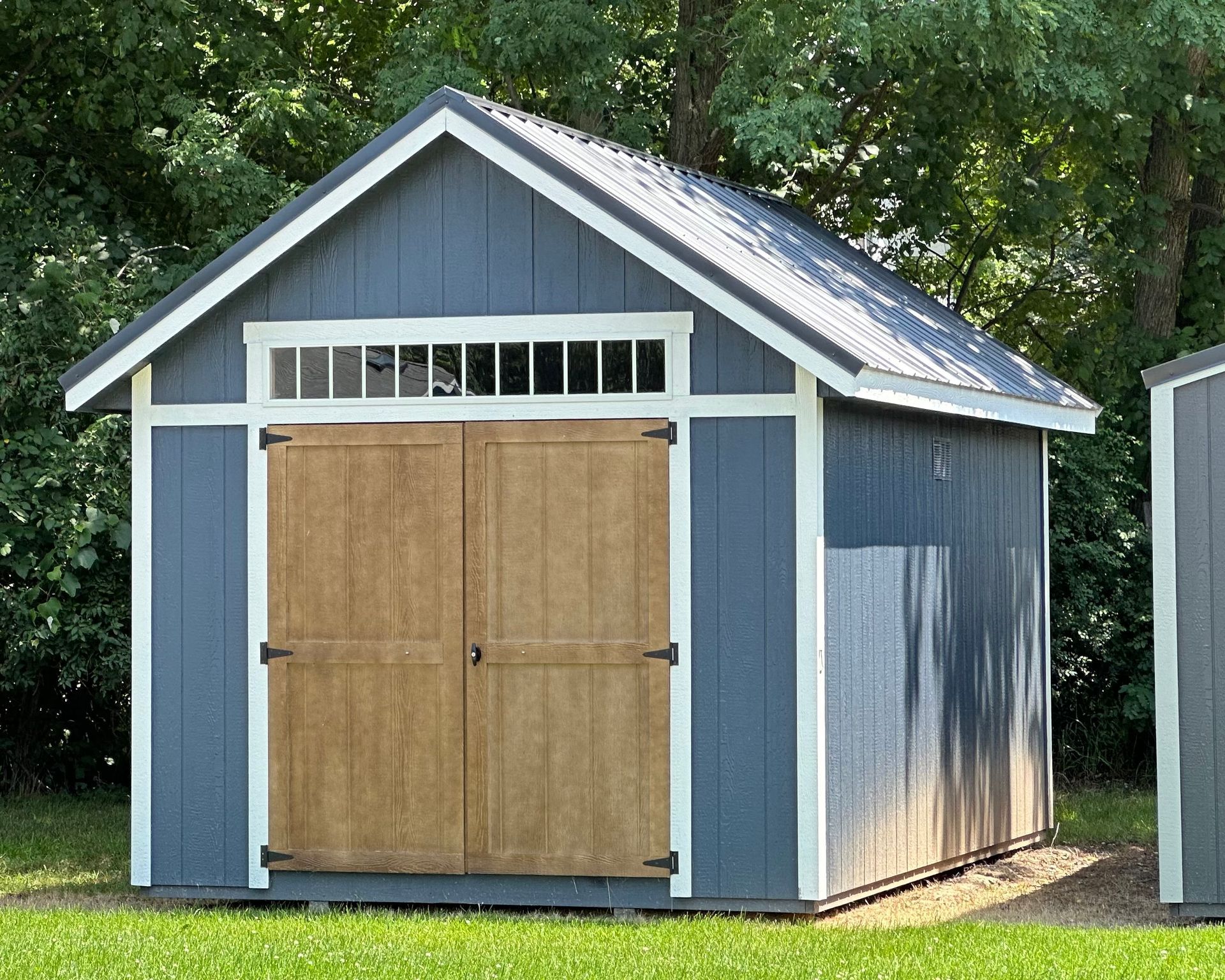 A blue and white shed with wooden doors is sitting in the grass.
