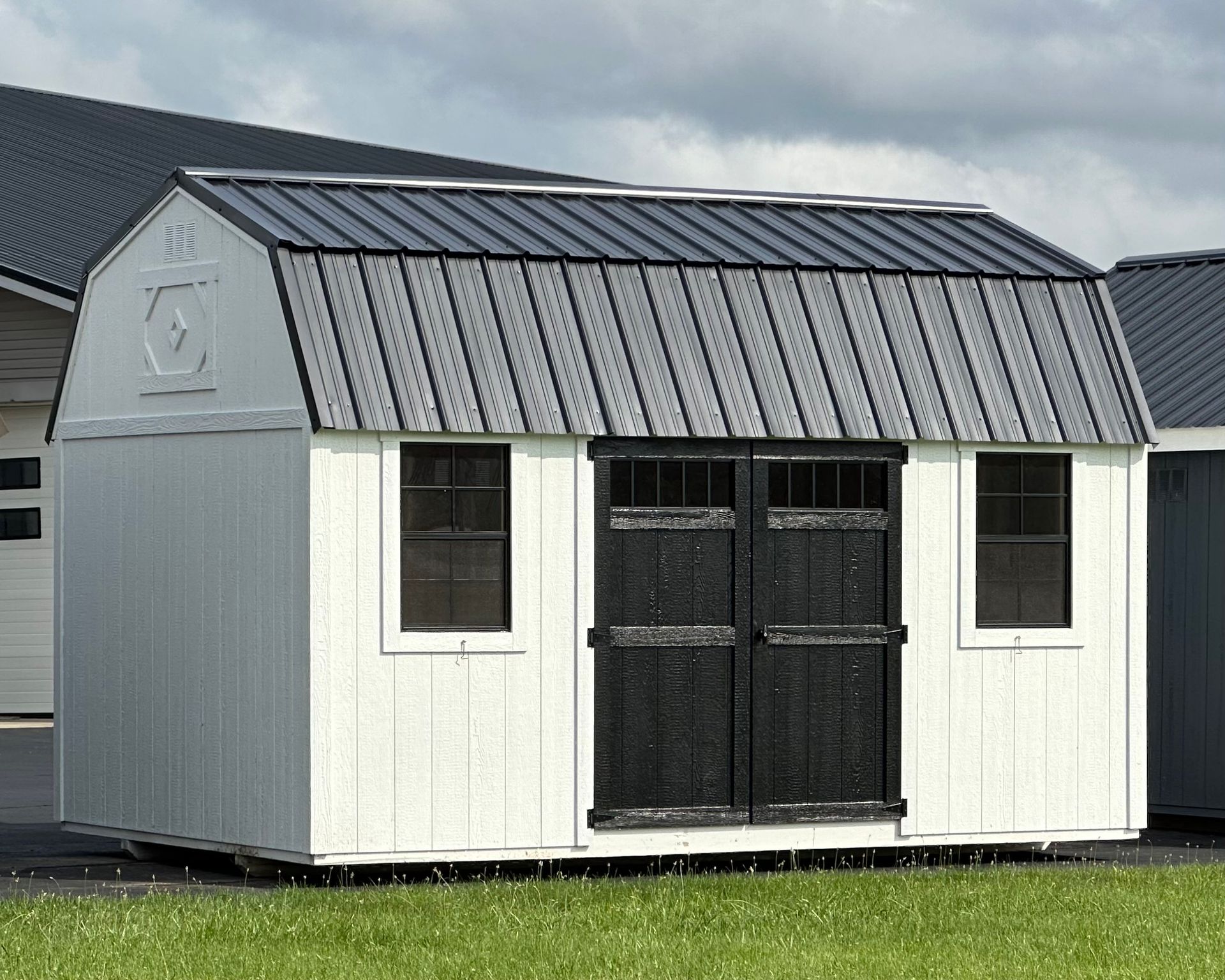 A white barn with a black roof is sitting on top of a lush green field.