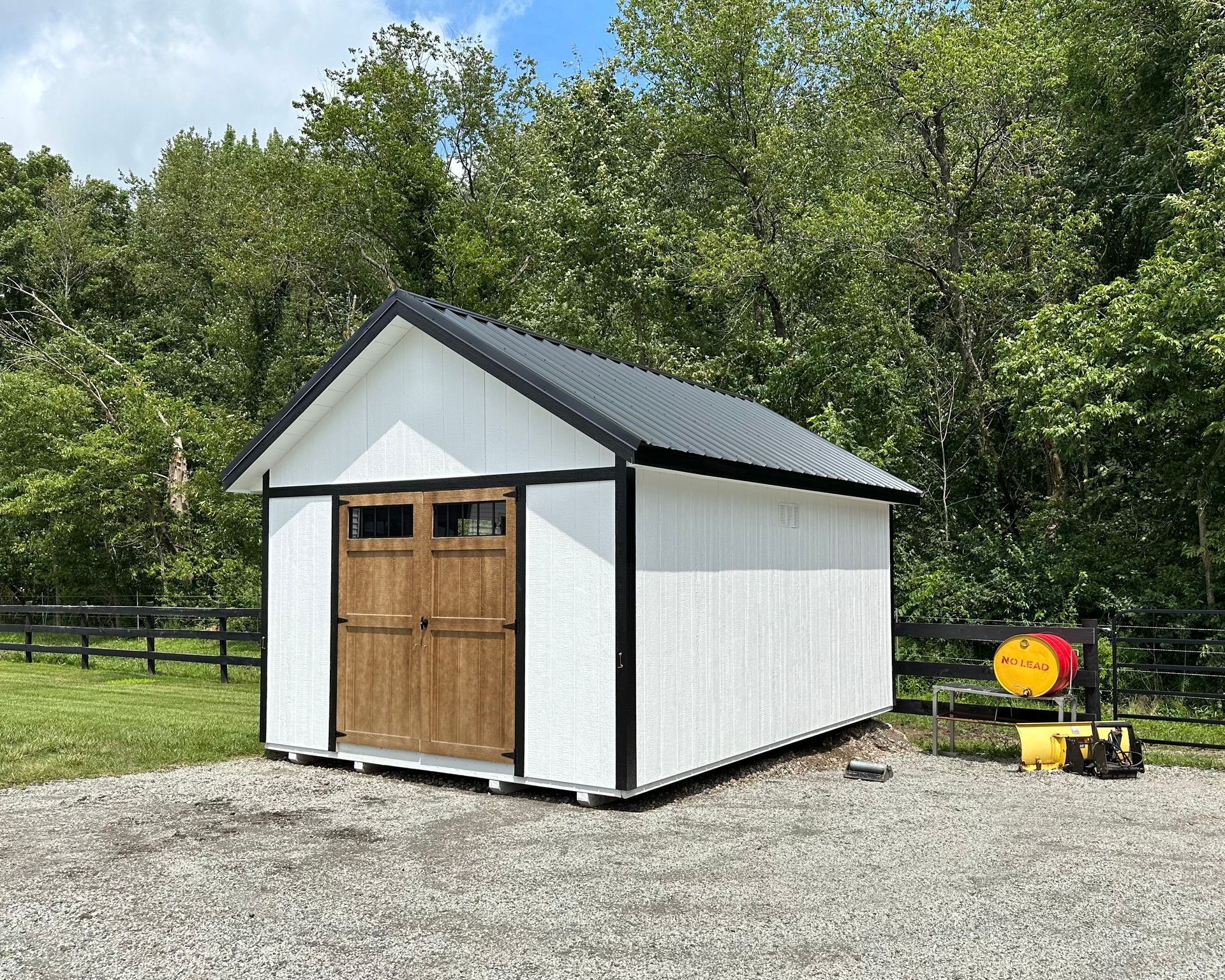 A white shed with a wooden door is sitting in the middle of a gravel driveway.