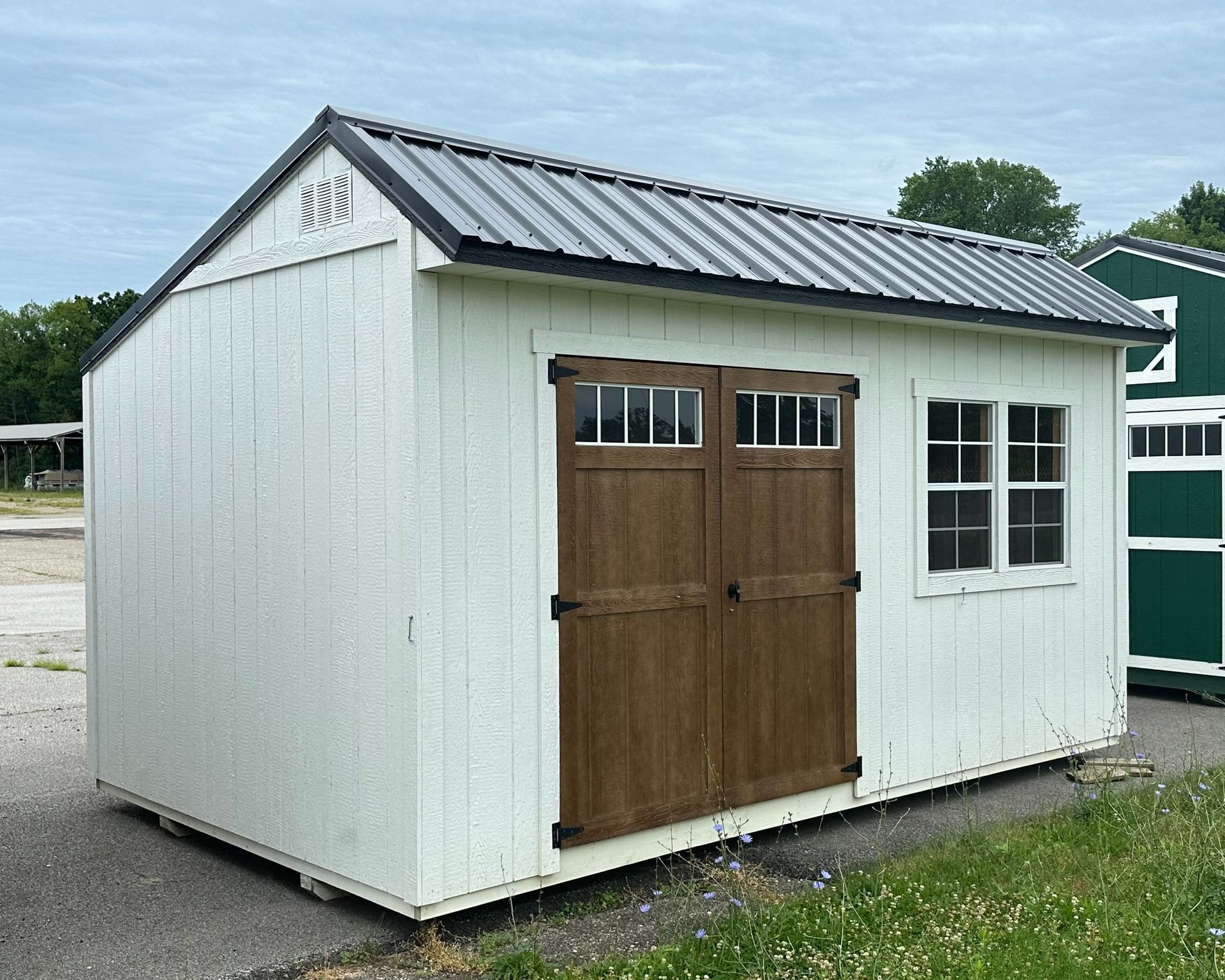 A white shed with a metal roof and wooden doors.