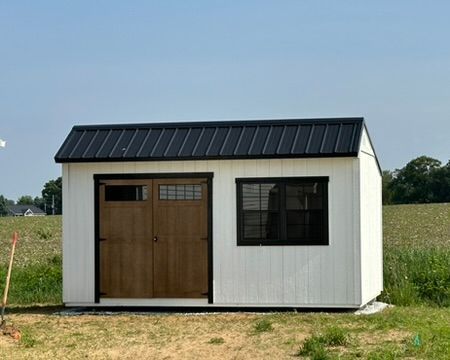 A white shed with a black roof is sitting in the middle of a field.