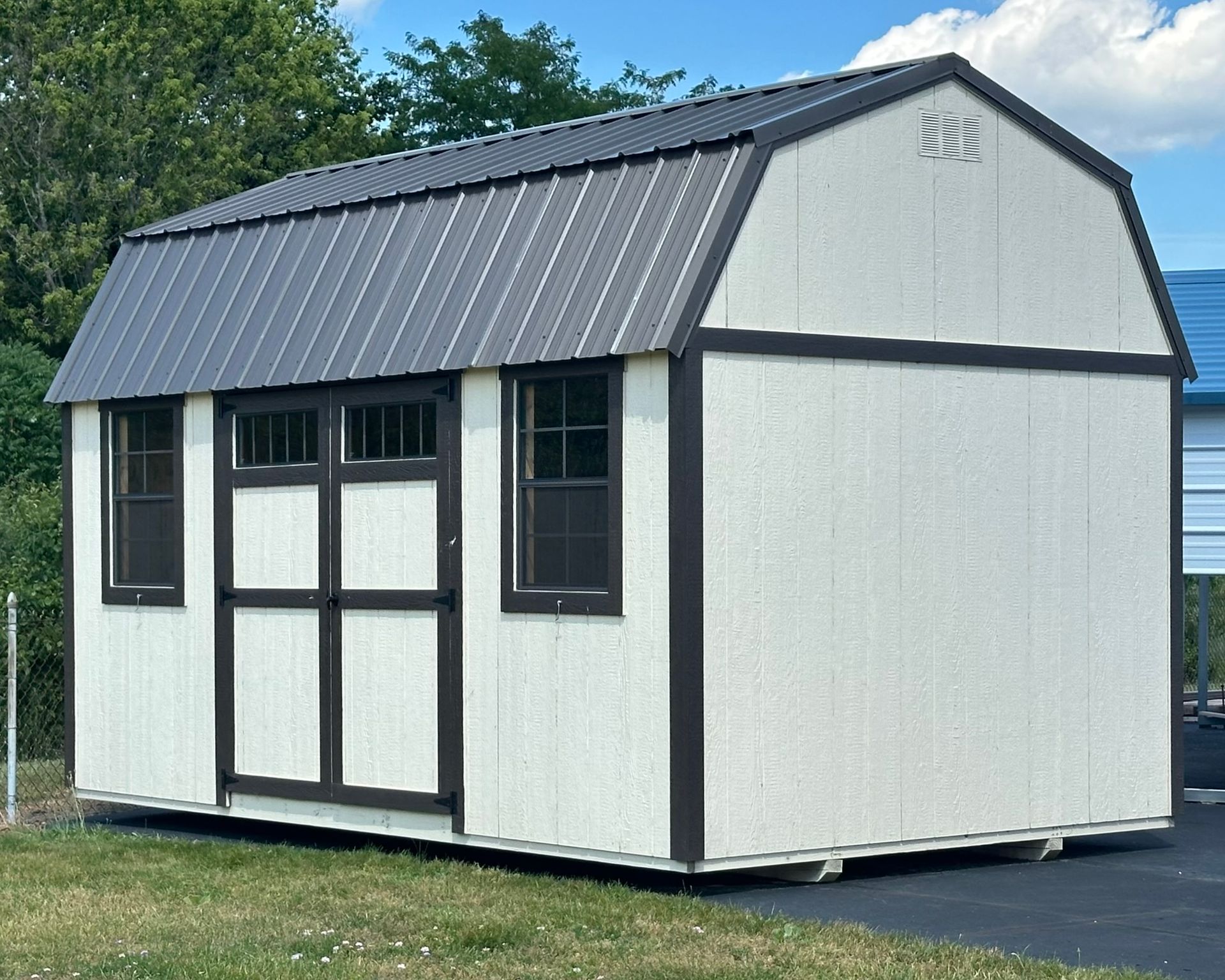 A white barn with a black roof is sitting in the middle of a grassy field.