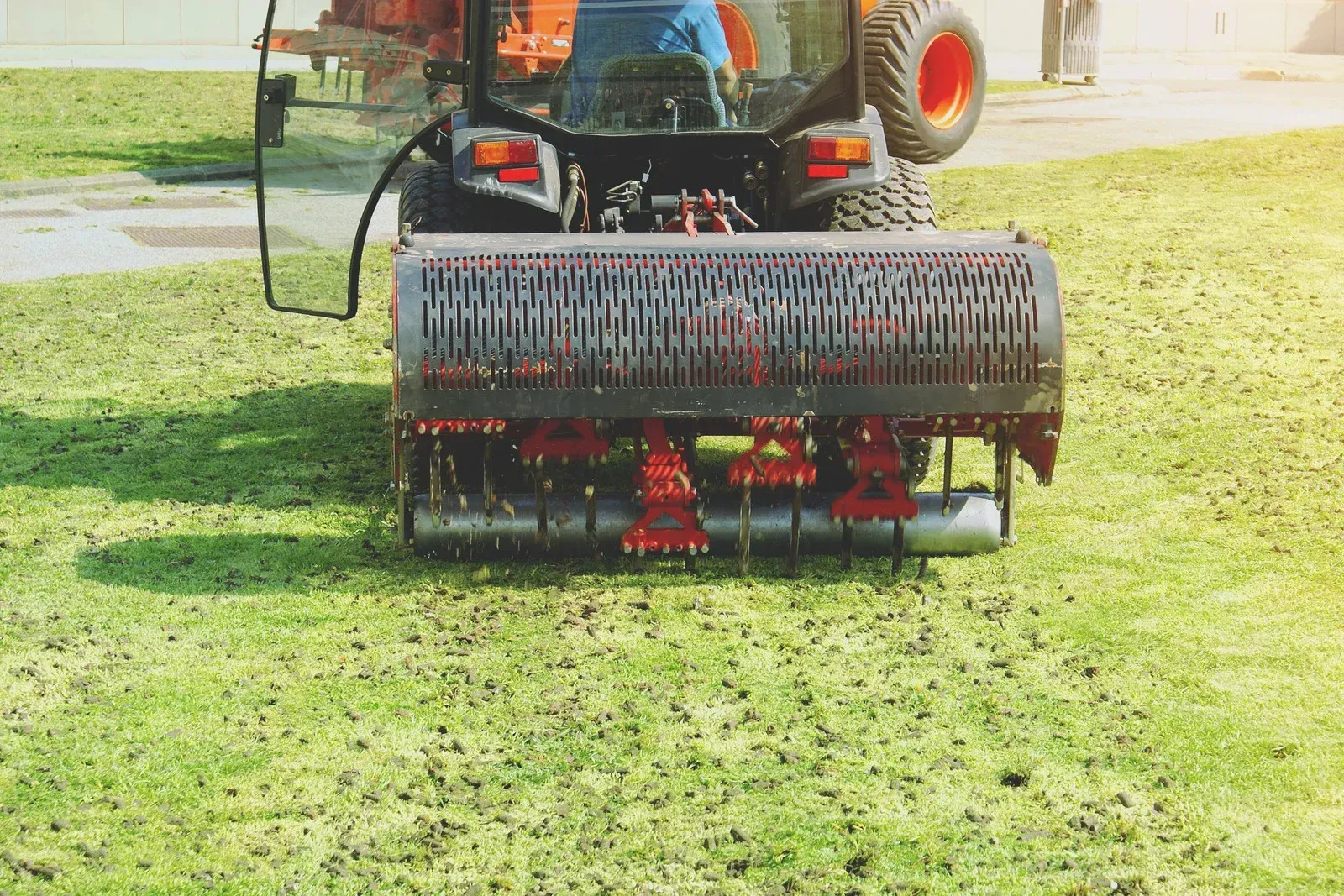 Person pushing an orange lawn mower on a dirt path, kicking up dust outdoors