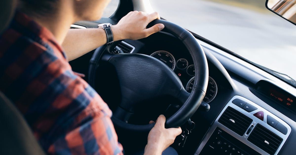 A man is driving a car with his hands on the steering wheel.