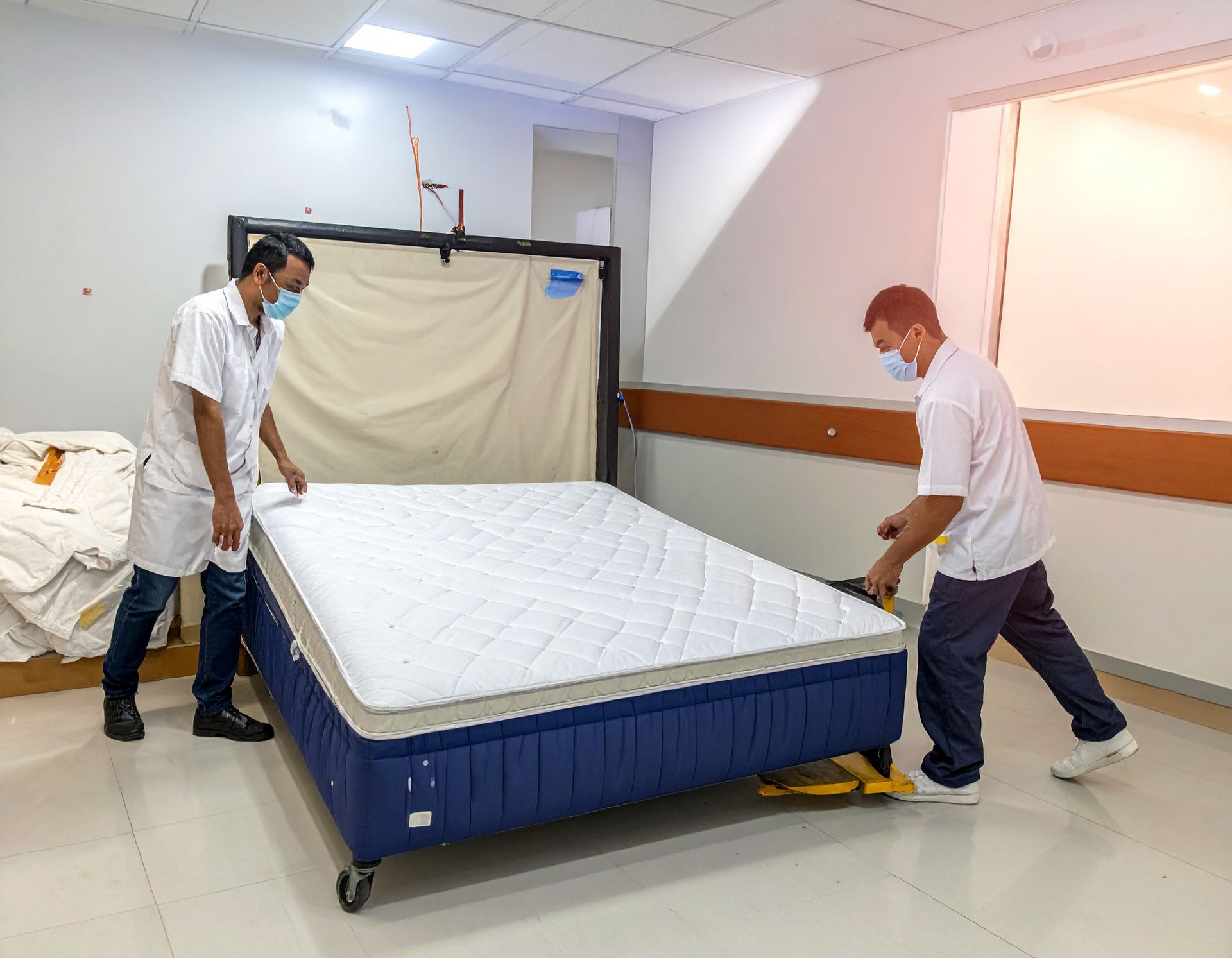 Two masked healthcare workers maneuvering a hospital bed, indoors.