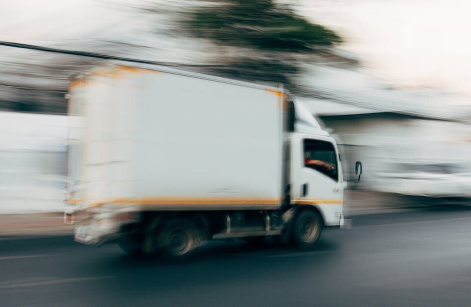 A white delivery truck is driving down a city street.