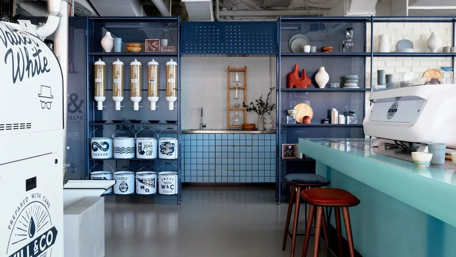 A kitchen with a counter , stools , shelves and a machine.