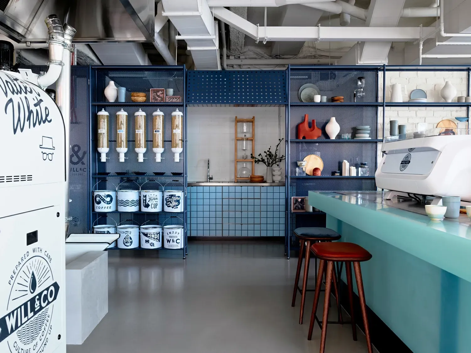 A kitchen with blue cabinets , shelves , a counter and stools.