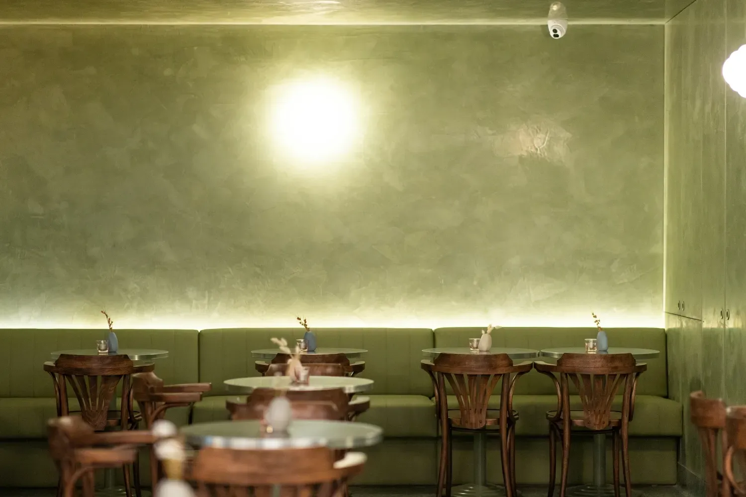 A restaurant with tables and chairs and a green wall.