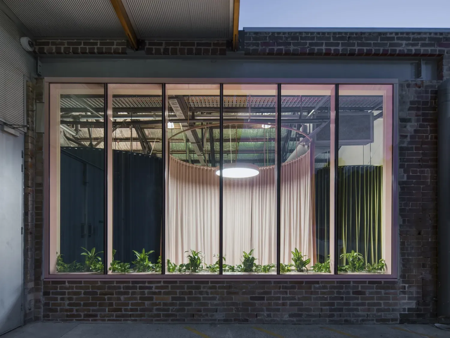 A large window in a brick building with plants growing out of it.