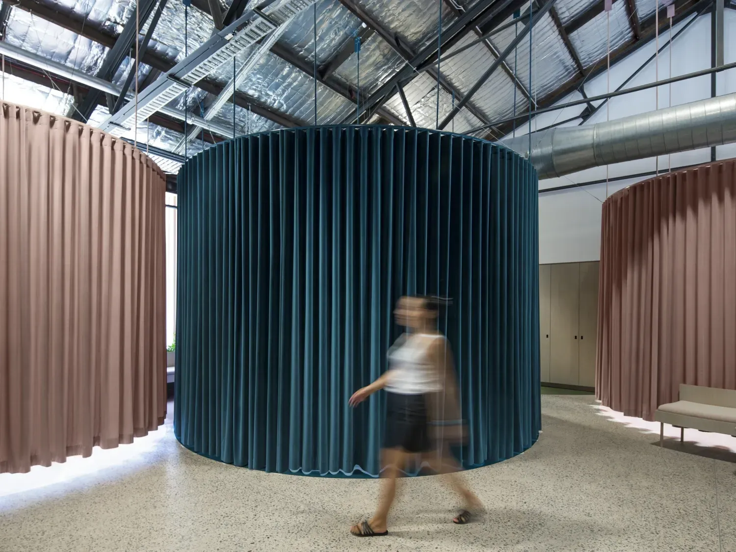 A woman is walking through a room with a blue curtain hanging from the ceiling.