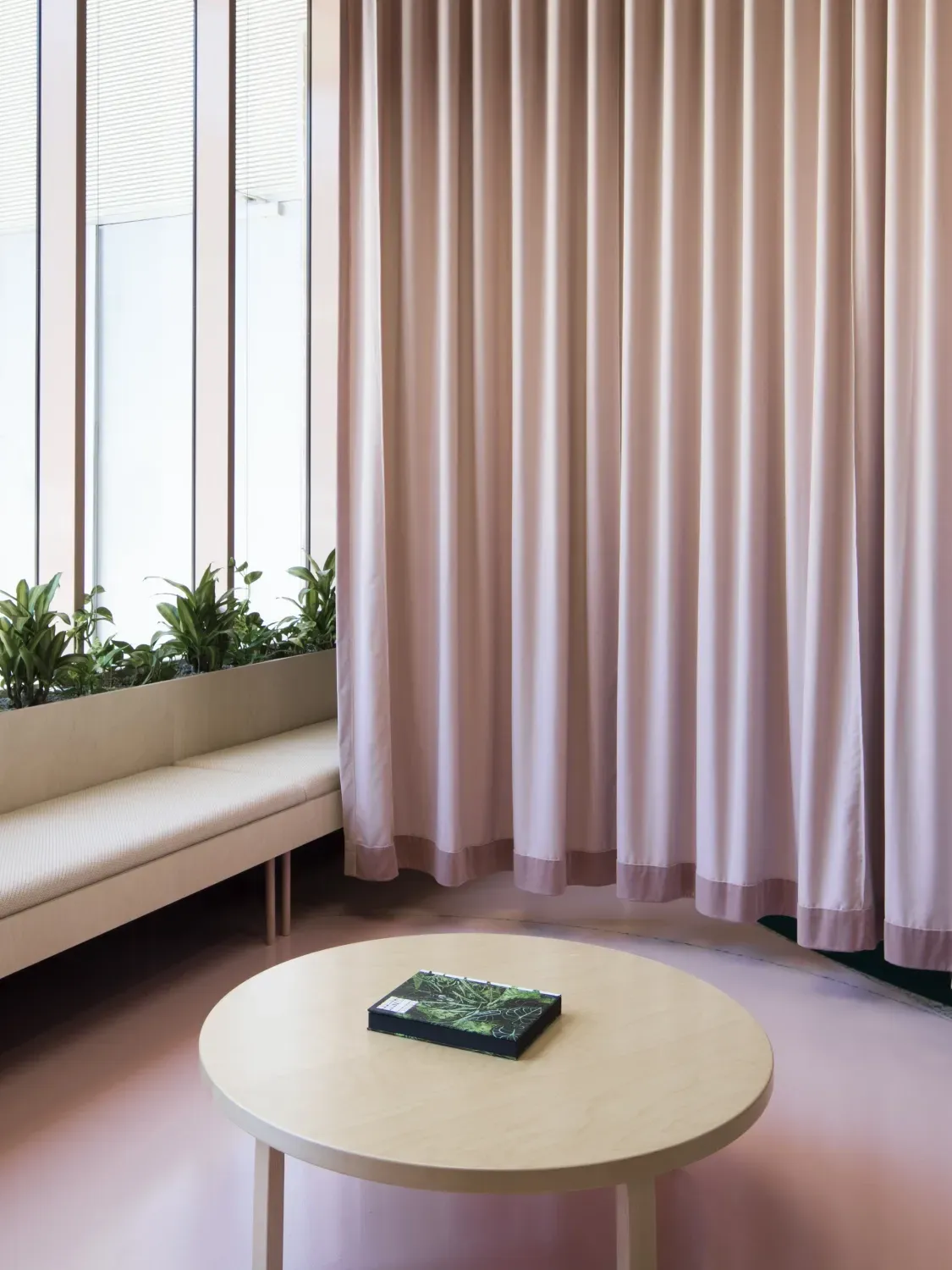 A round table is sitting in front of a window in a room with pink curtains.
