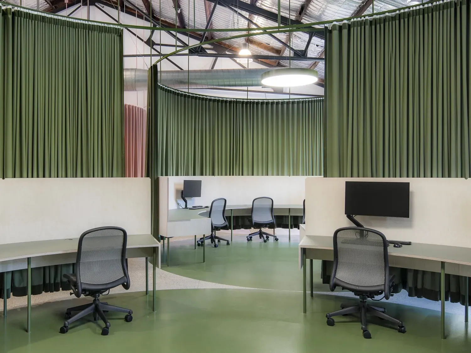 A room with a lot of desks and chairs and green curtains.