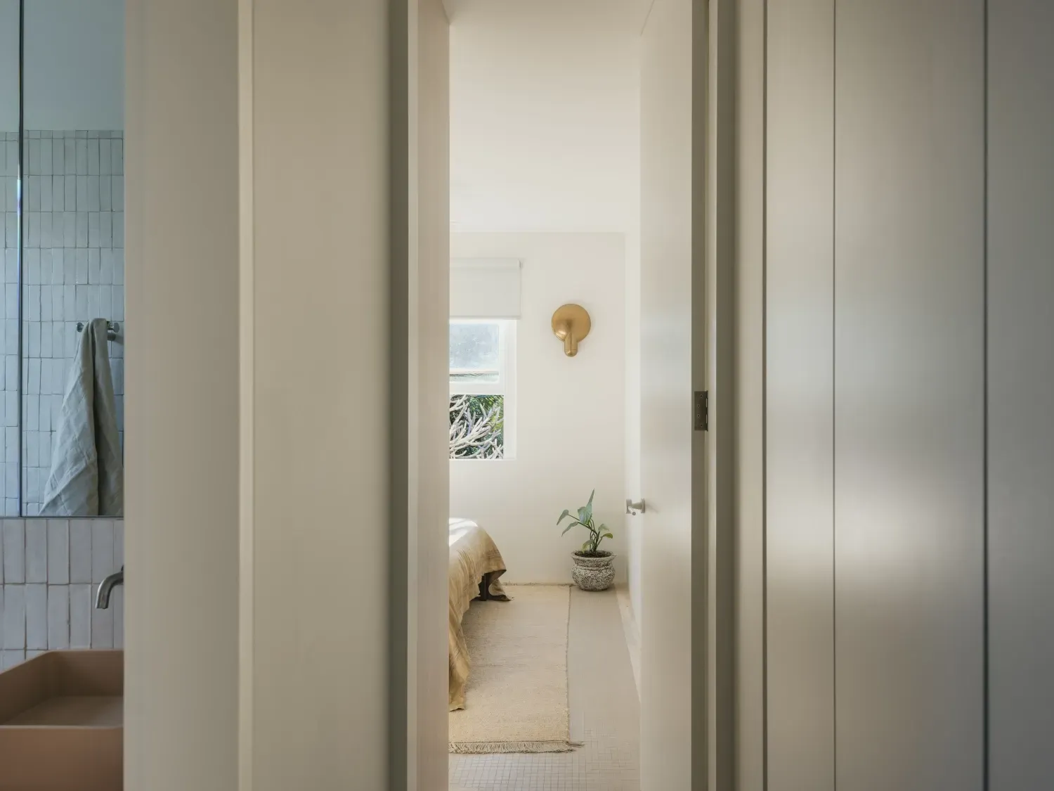 A hallway leading to a bedroom with a sink and a window.