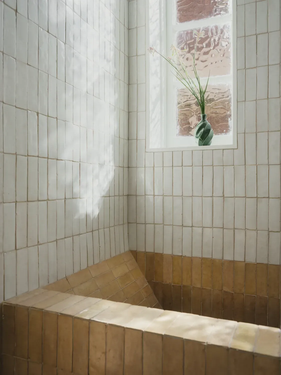 A bathtub in a bathroom with a window and a plant in a vase