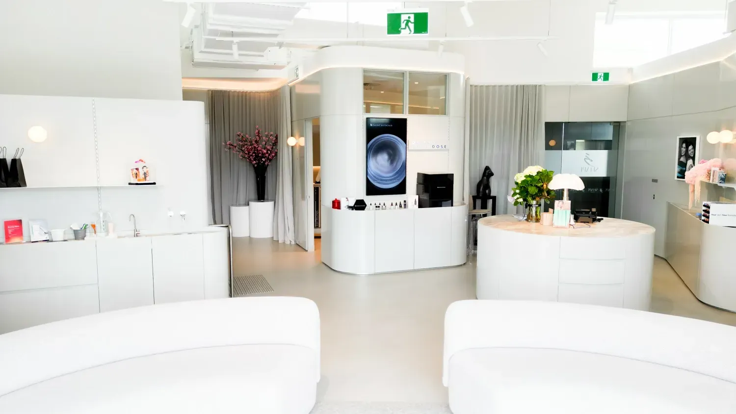 A living room with white furniture and a green exit sign.