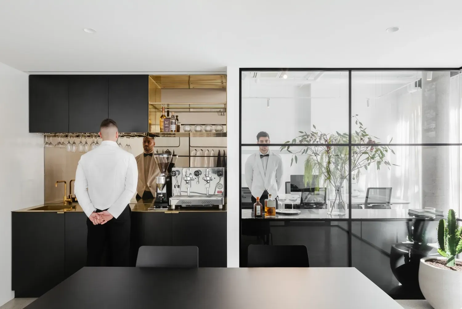 A man in a white shirt is standing in a kitchen next to a table.
