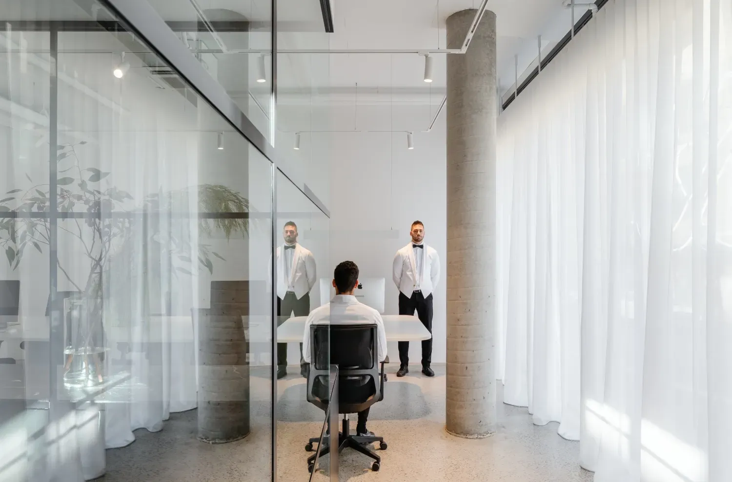 A man is sitting in an office chair in front of a glass wall.