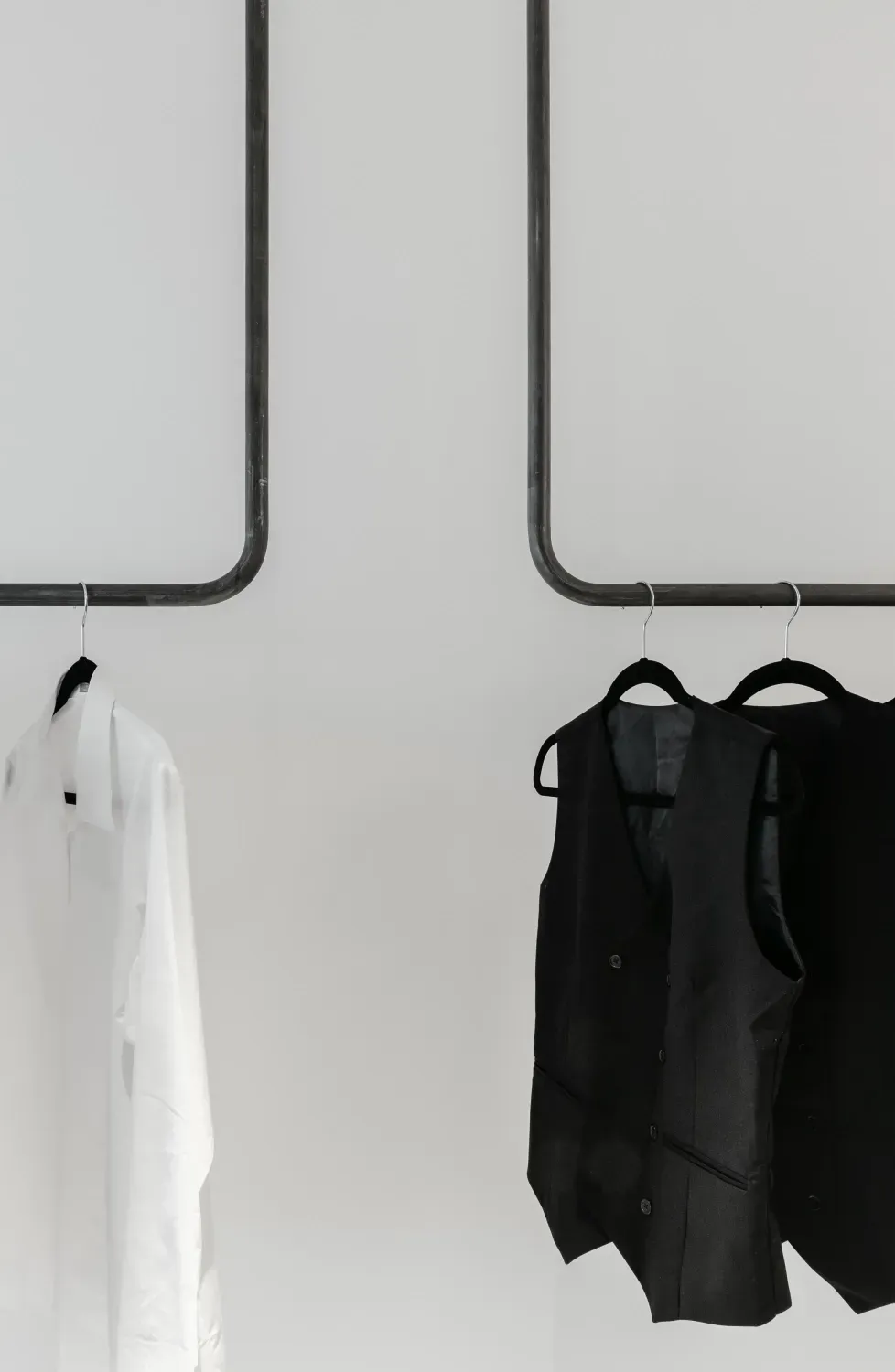 A white shirt and a black vest are hanging on a rack.