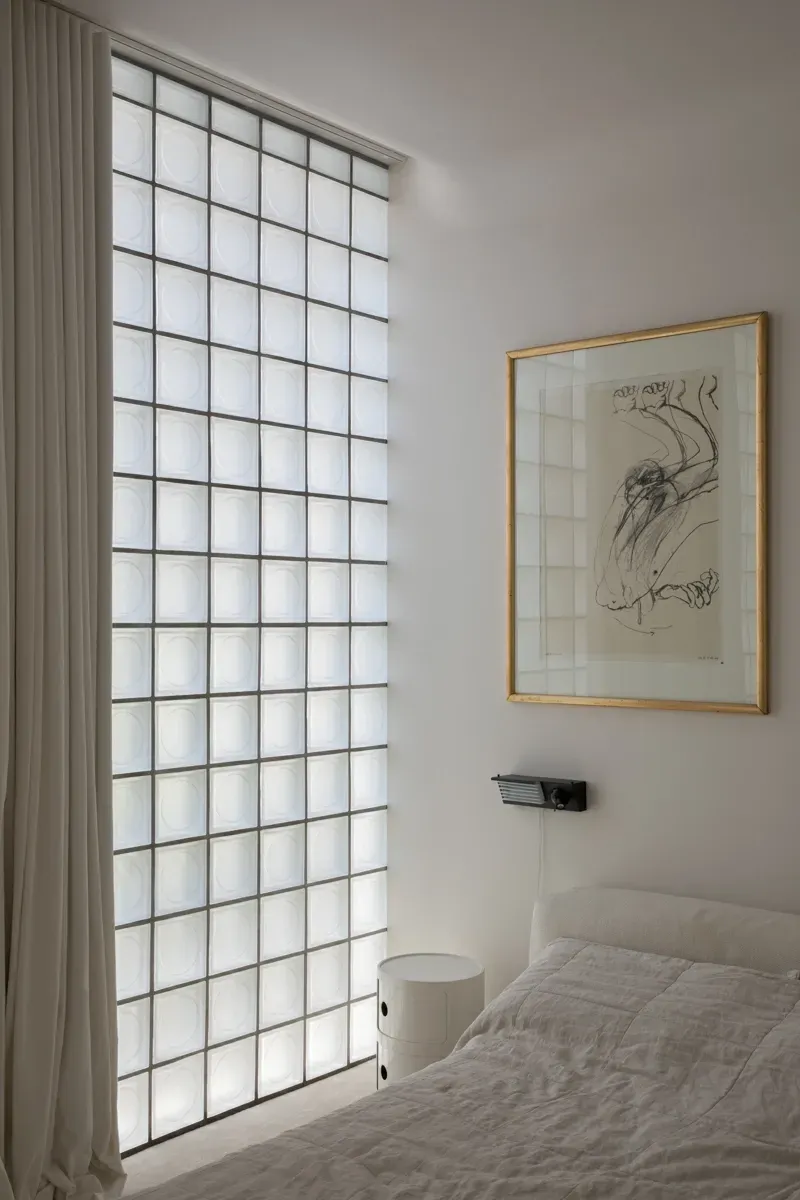 A bedroom with a glass wall and a picture on the wall above the bed.