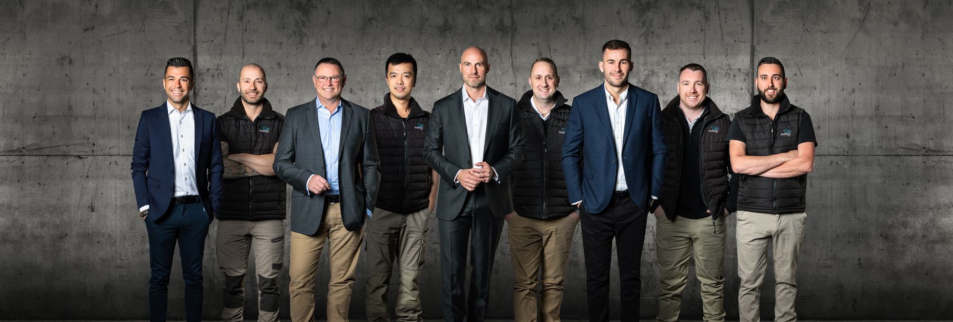 A group of men are standing next to each other in front of a concrete wall.