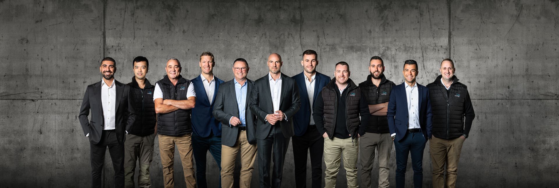 A group of men are standing next to each other in front of a concrete wall.
