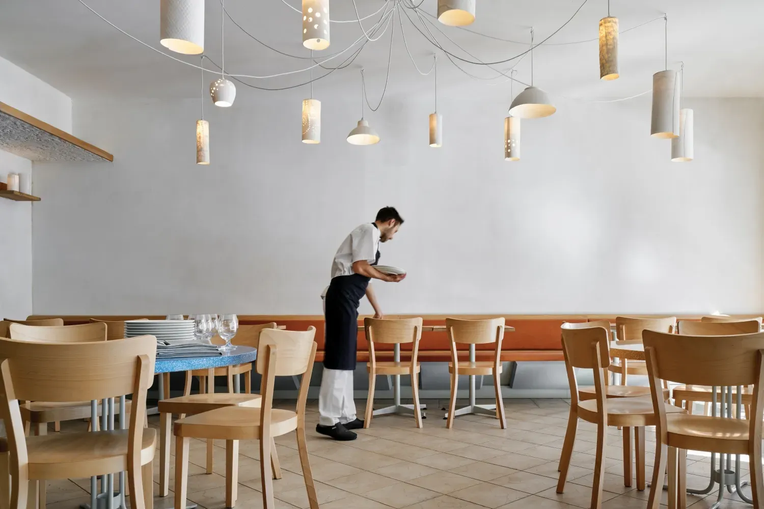 A man is standing in a restaurant setting tables and chairs.