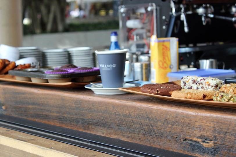 A cup of coffee is sitting on a wooden counter next to a tray of cookies.
