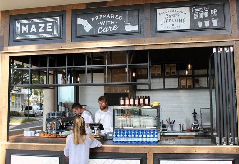 A woman stands at a counter in front of a sign that says maze prepared with care