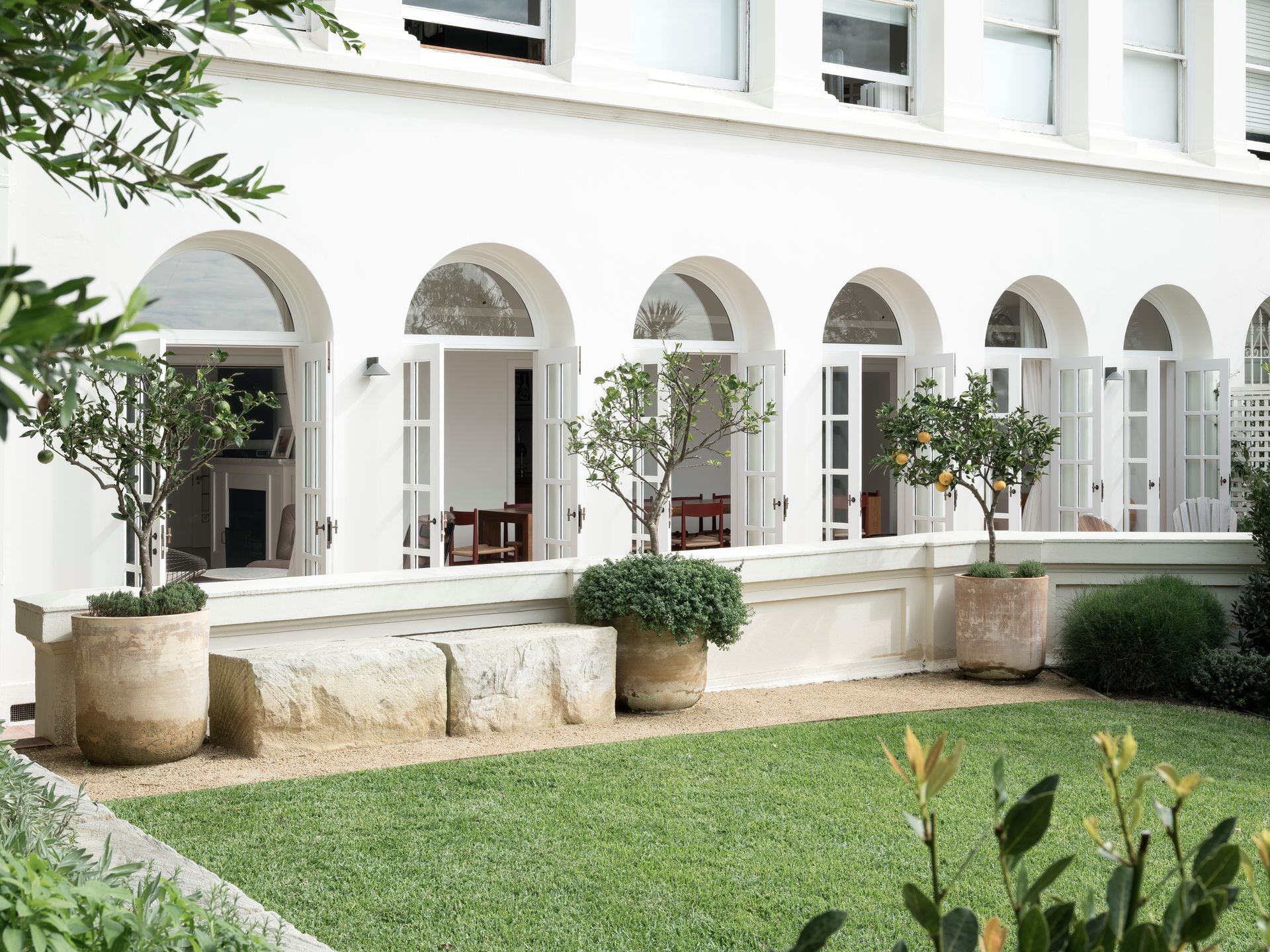 A white building with arched windows and potted plants in front of it.