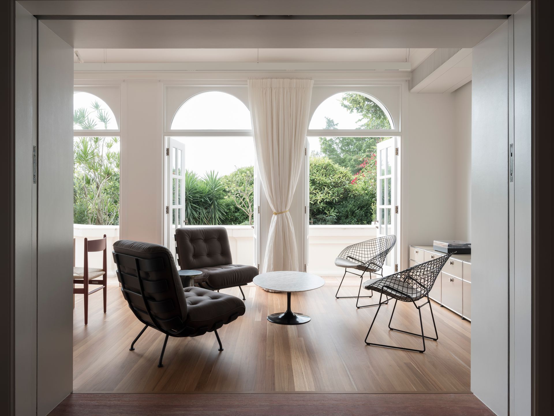 A living room with chairs , a table , and arched windows.
