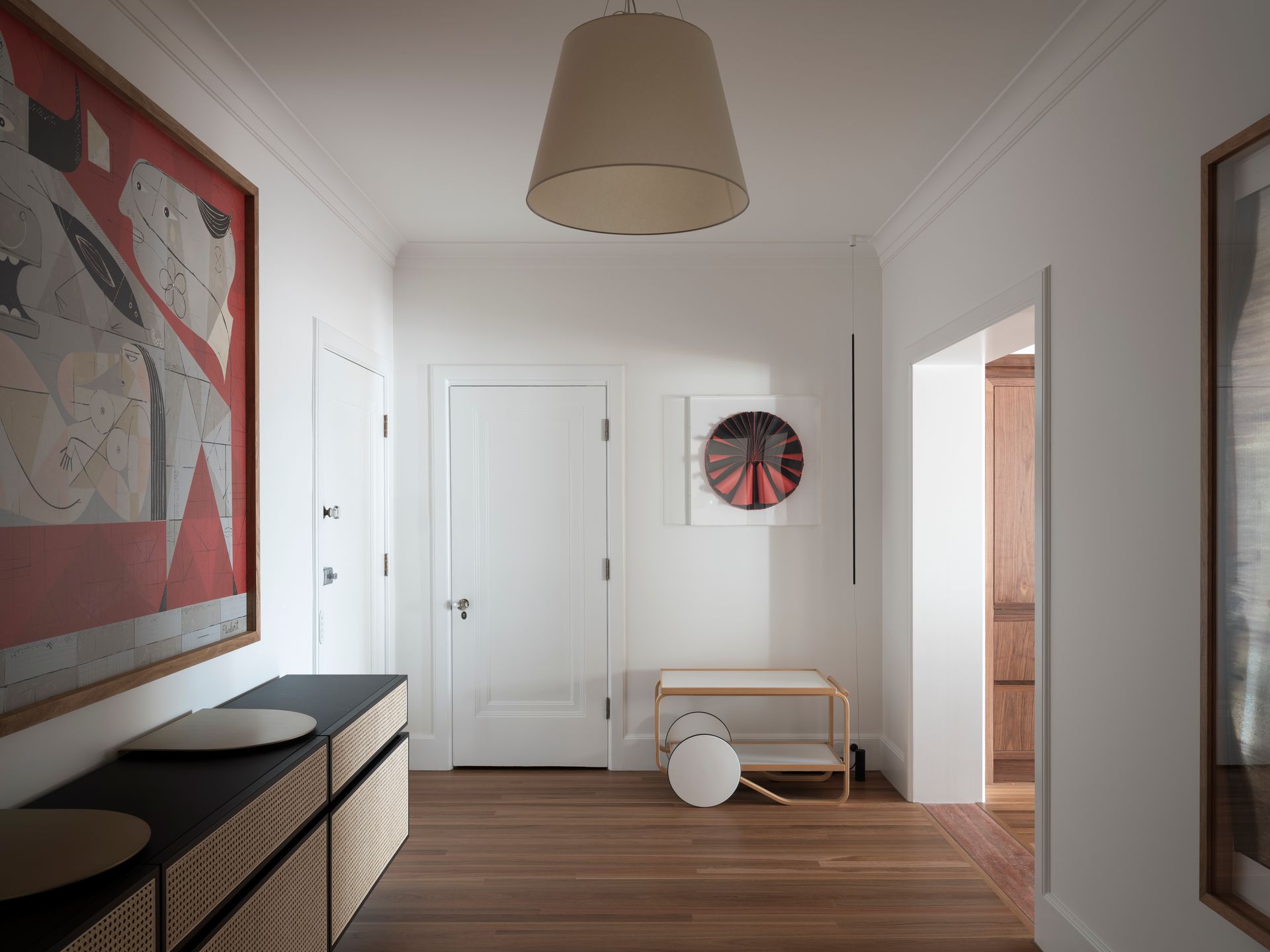 A hallway with a painting on the wall and a lamp hanging from the ceiling.