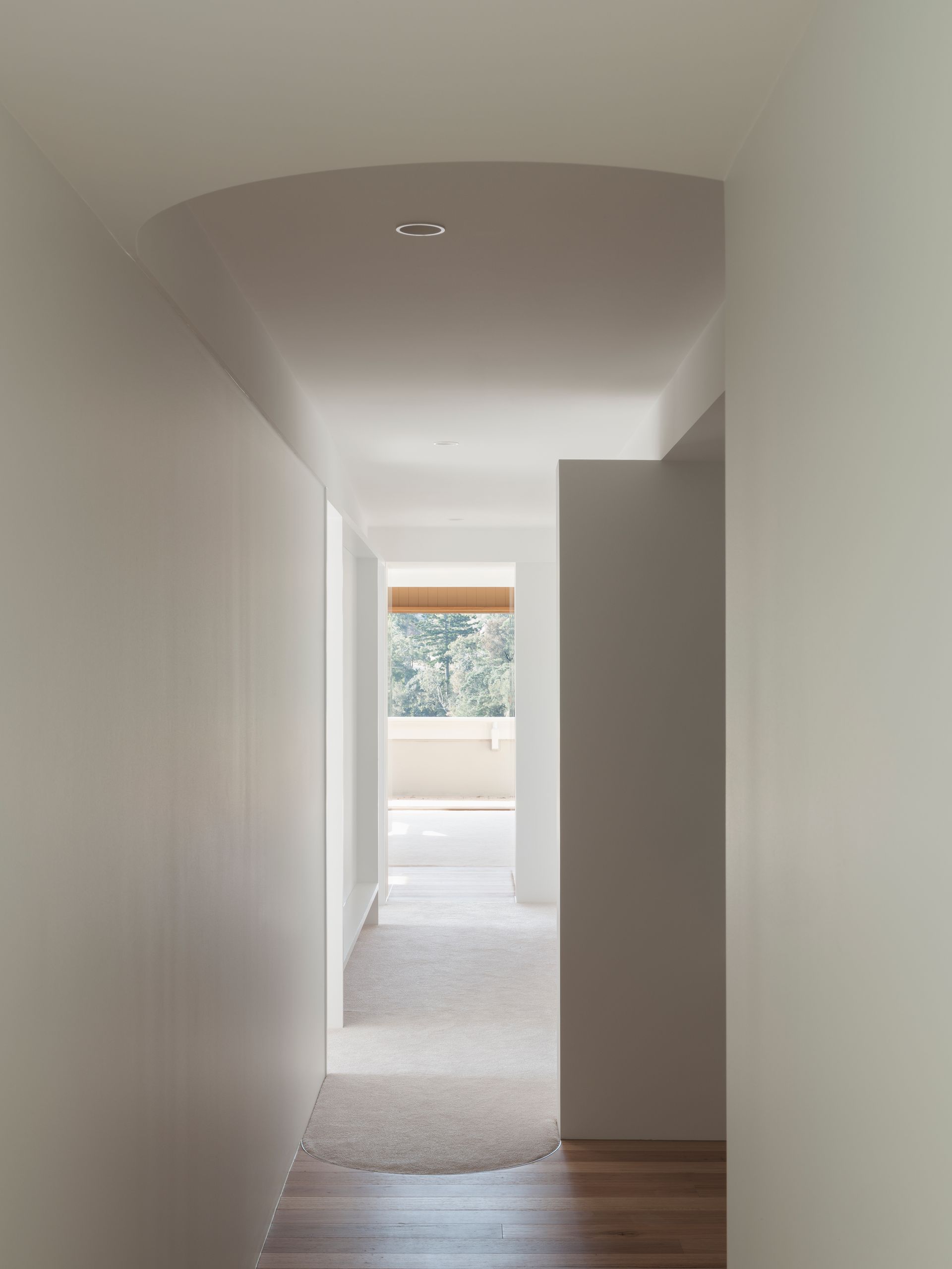 A long hallway with white walls and wooden floors leading to a bedroom.