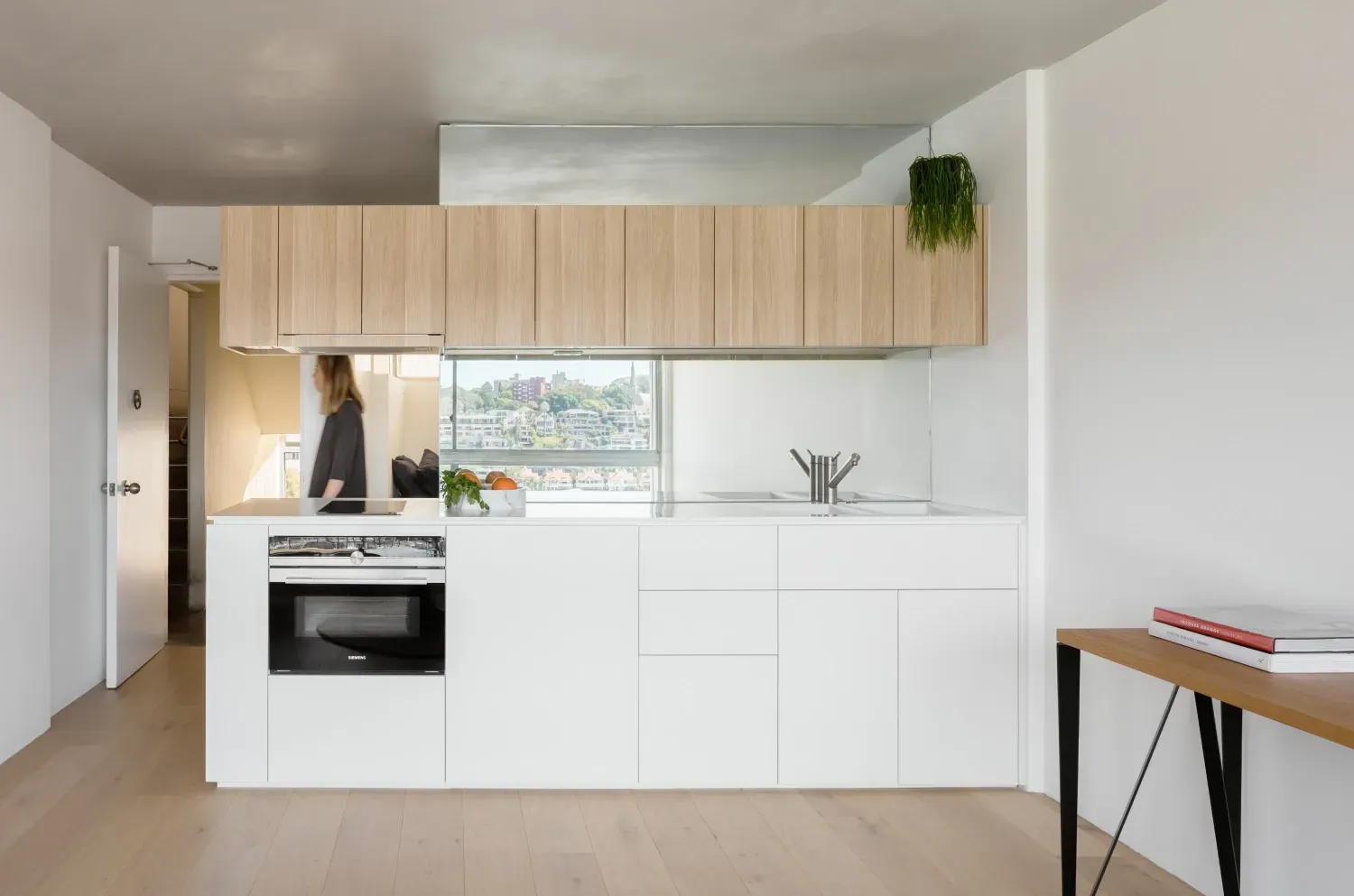 A woman is standing in a kitchen with white cabinets and wooden cabinets.