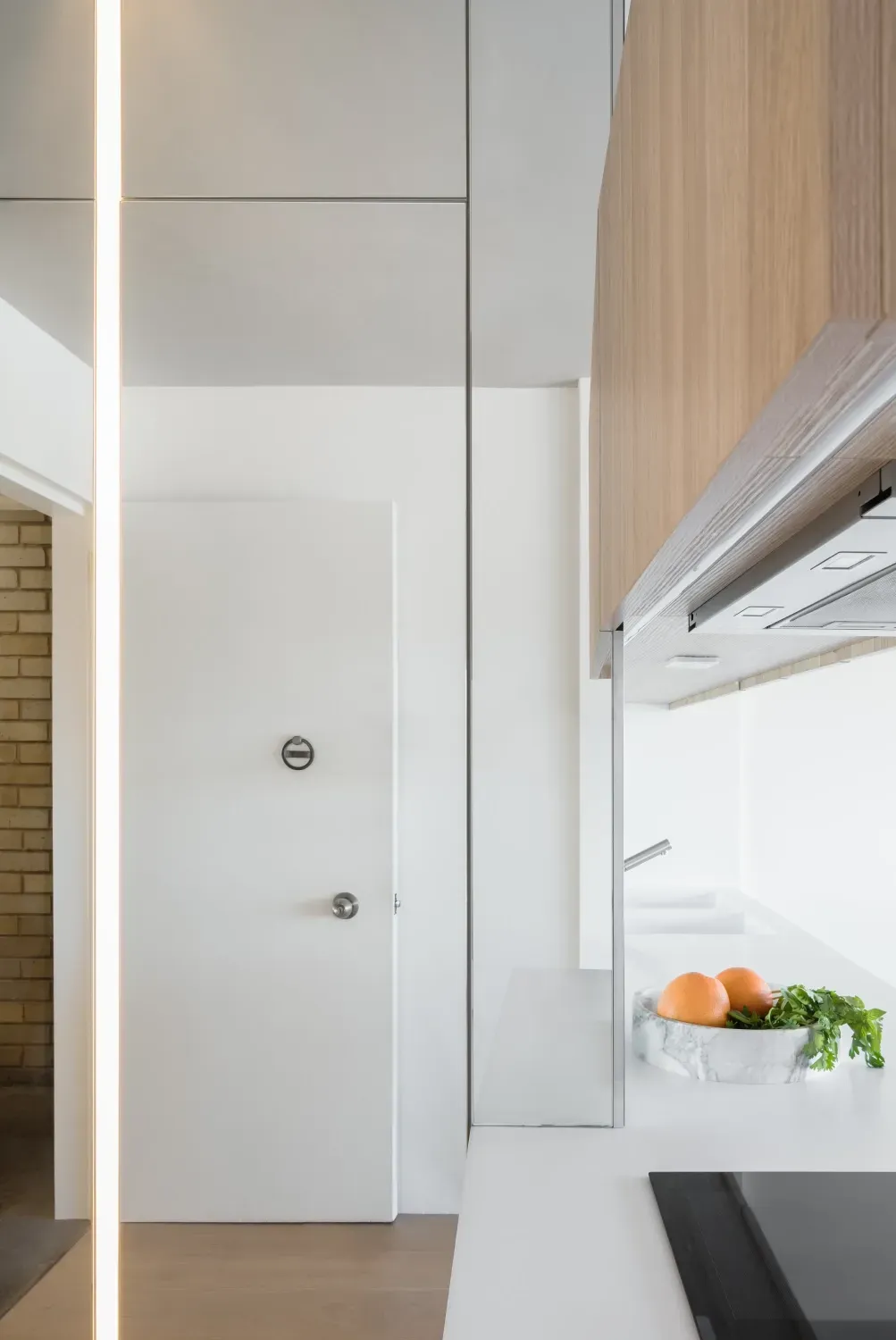A kitchen with a white door and wooden cabinets and a bowl of fruit on the counter.